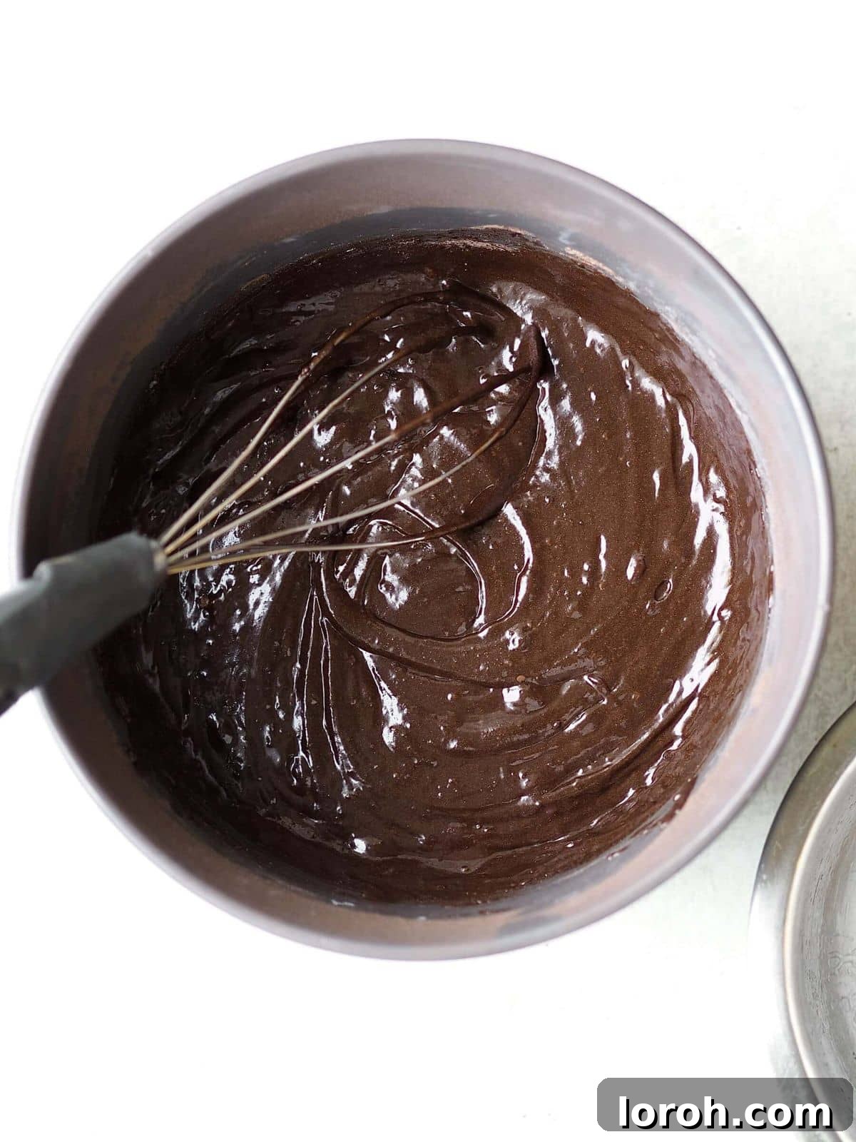 A bowl containing chocolate cake mix being whisked to achieve a smooth batter.
