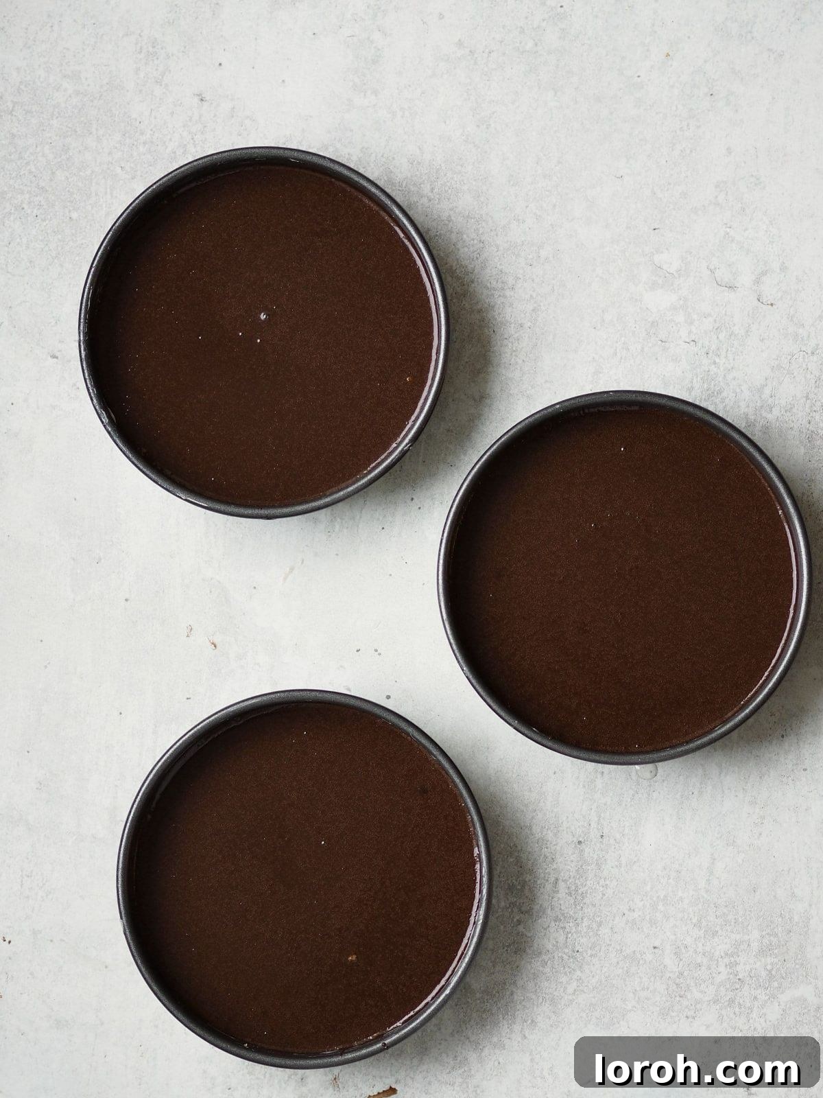 Chocolate cake batter being poured into a prepared round cake tin.