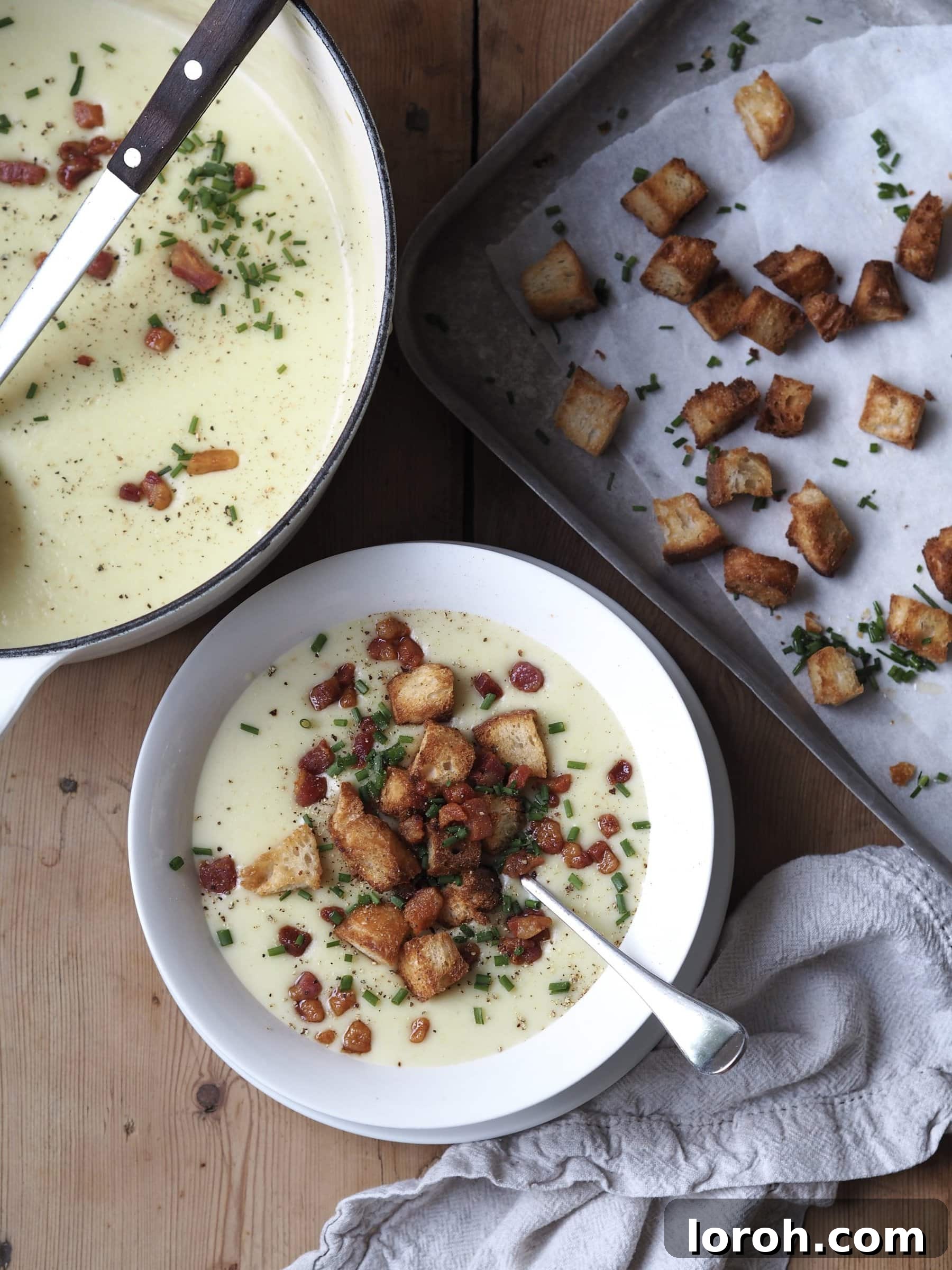 A hand serving a bowl of Creamy Leek and Potato Soup garnished with fresh chives and black pepper.