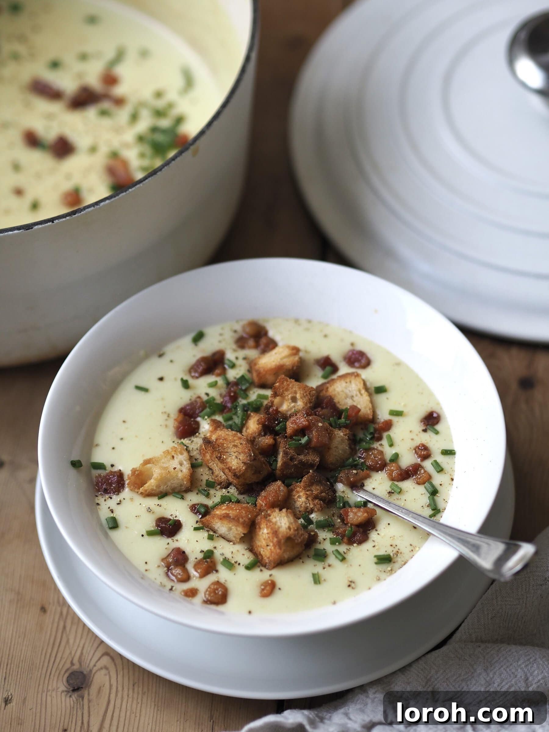 Full bowl of Creamy Potato and Leek Soup with bacon, croutons, and chives, ready to eat.