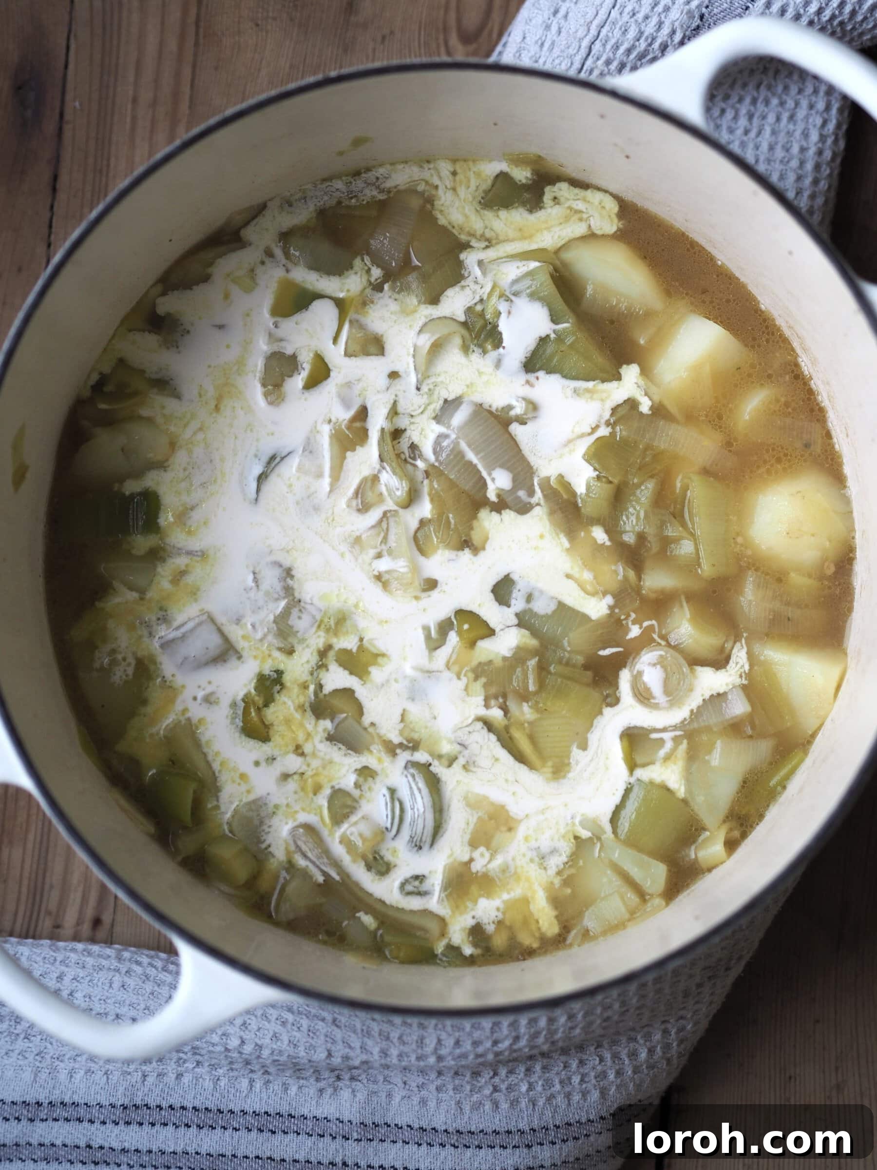 Stirring double cream into the softened potato and leek mixture.