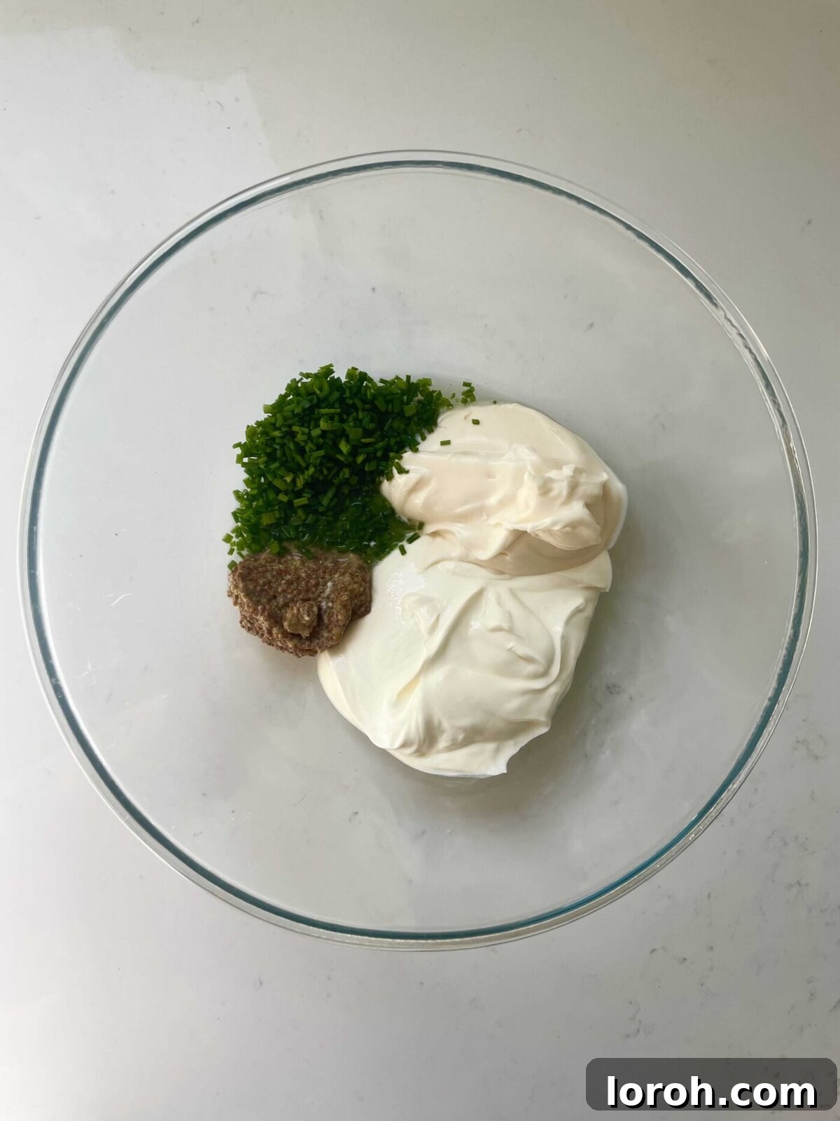 Zesty Celeriac Remoulade 5 A bowl containing a creamy, yellow dressing, with chives visible, being mixed with a whisk for the celeri remoulade recipe.