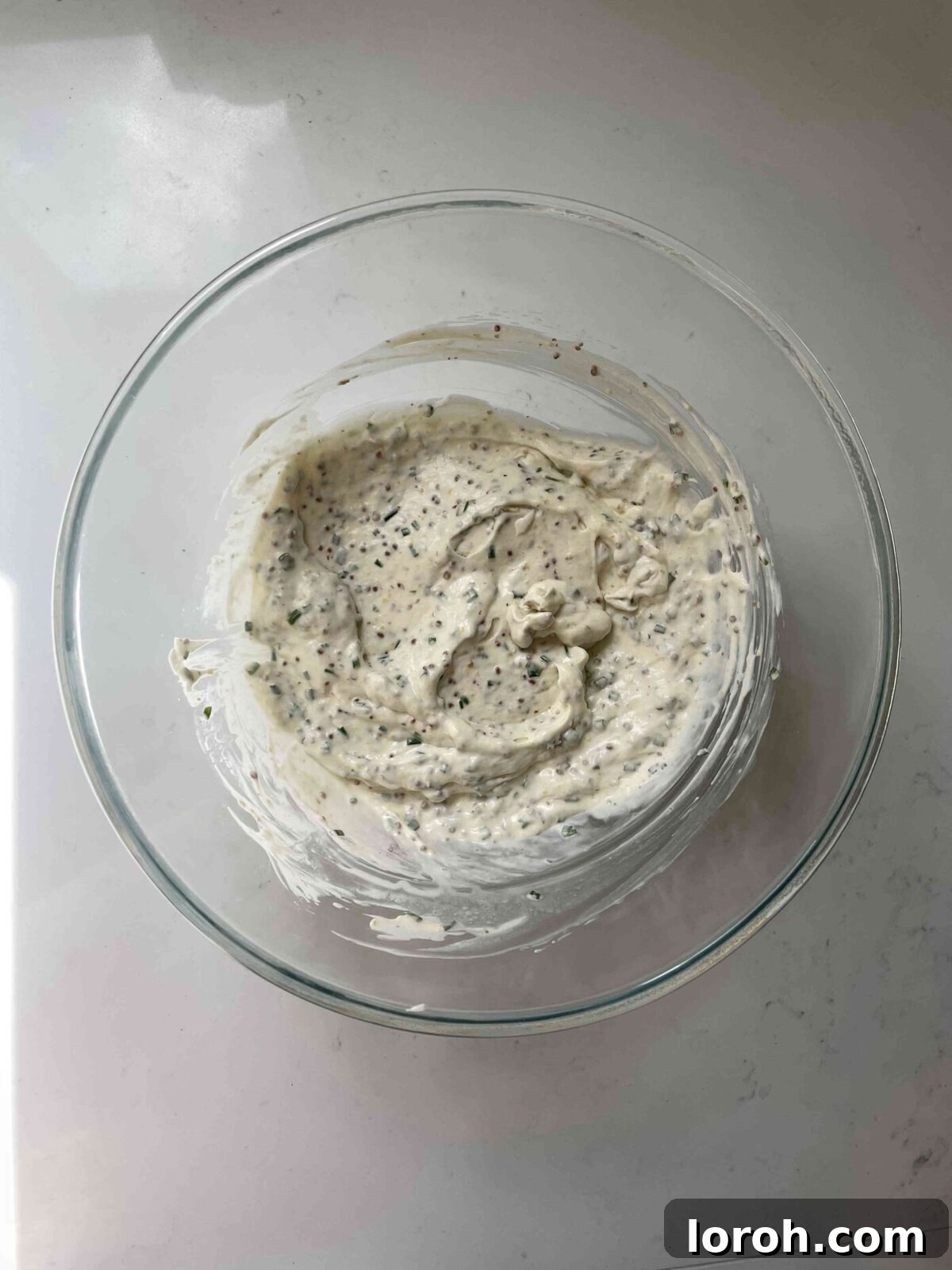 Zesty Celeriac Remoulade 6 A smooth, creamy, yellow dressing, flecked with green chives and mustard seeds, resting in a glass bowl after being mixed for celeri remoulade.