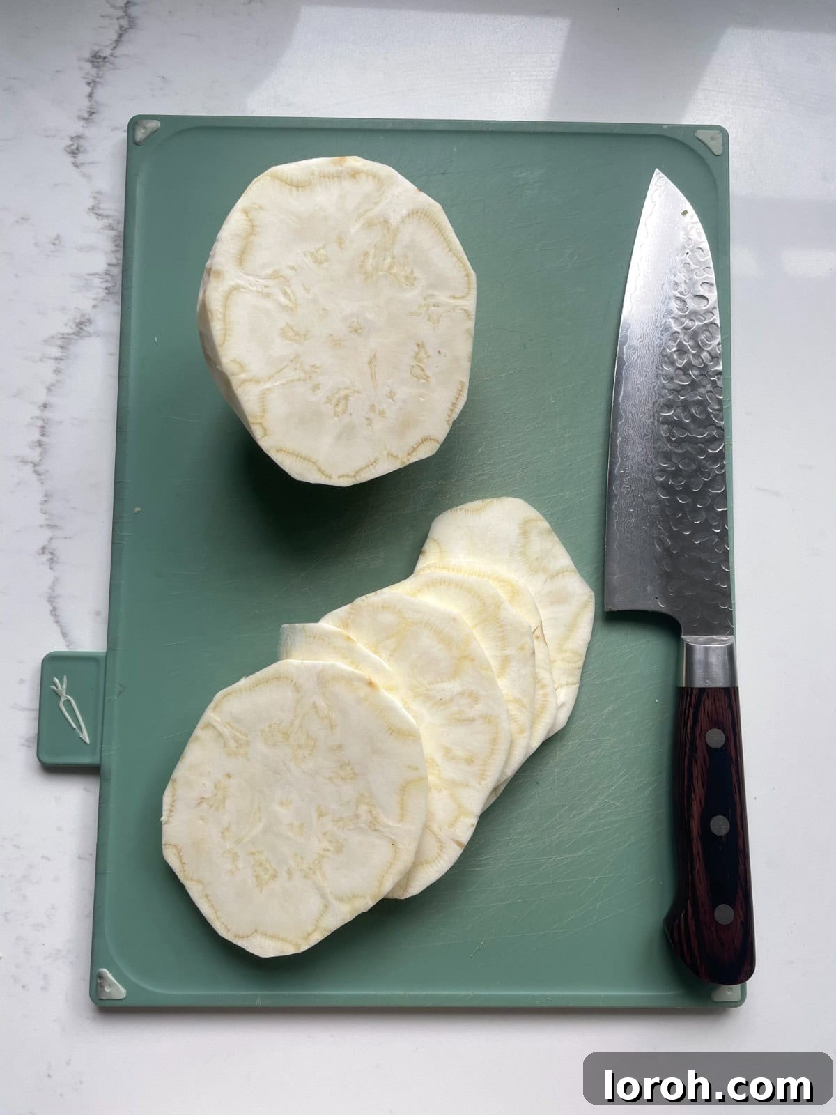 Zesty Celeriac Remoulade 8 A celeriac bulb being thinly sliced into uniform 5mm discs on a wooden cutting board with a sharp knife, preparing it for celeri remoulade.