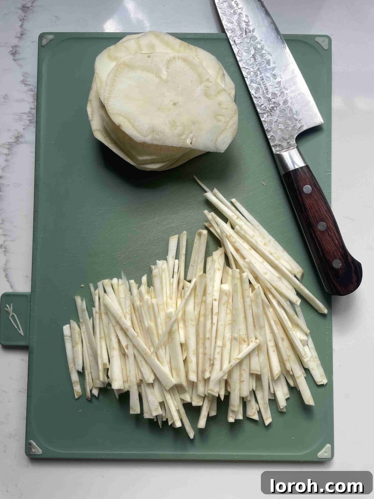 Zesty Celeriac Remoulade 9 Thin celeriac discs being further sliced into delicate matchsticks on a wooden cutting board, showcasing the precise preparation for celeri remoulade.