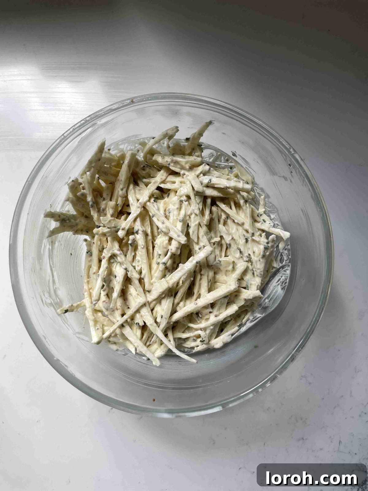 Zesty Celeriac Remoulade 10 A vibrant celeri remoulade, with crunchy celeriac matchsticks fully coated in a creamy, mustard-mayonnaise dressing, presented in a glass bowl.