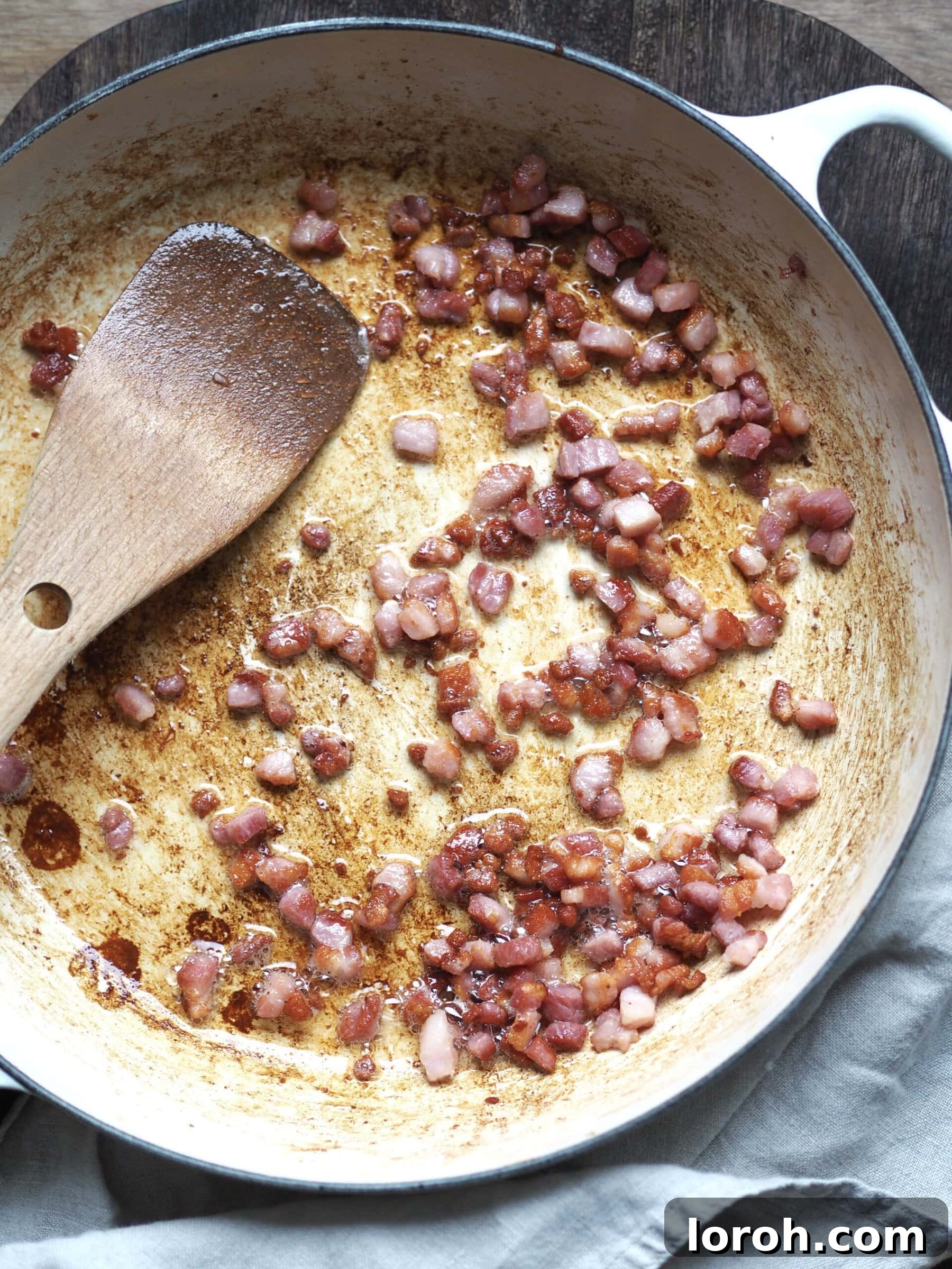 Bacon lardons frying in a white shallow casserole dish.