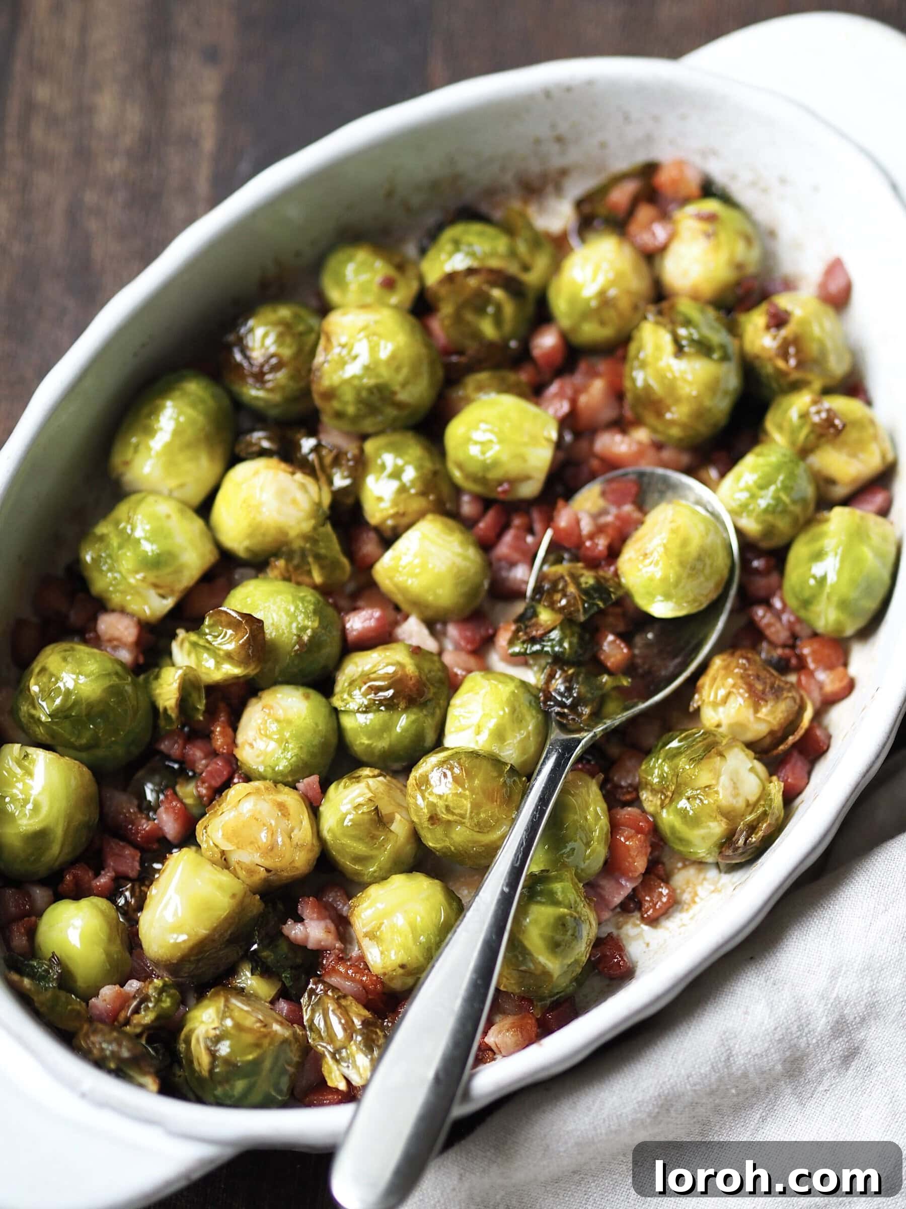 White serving dish with whole roasted sprouts with bacon lardons.
