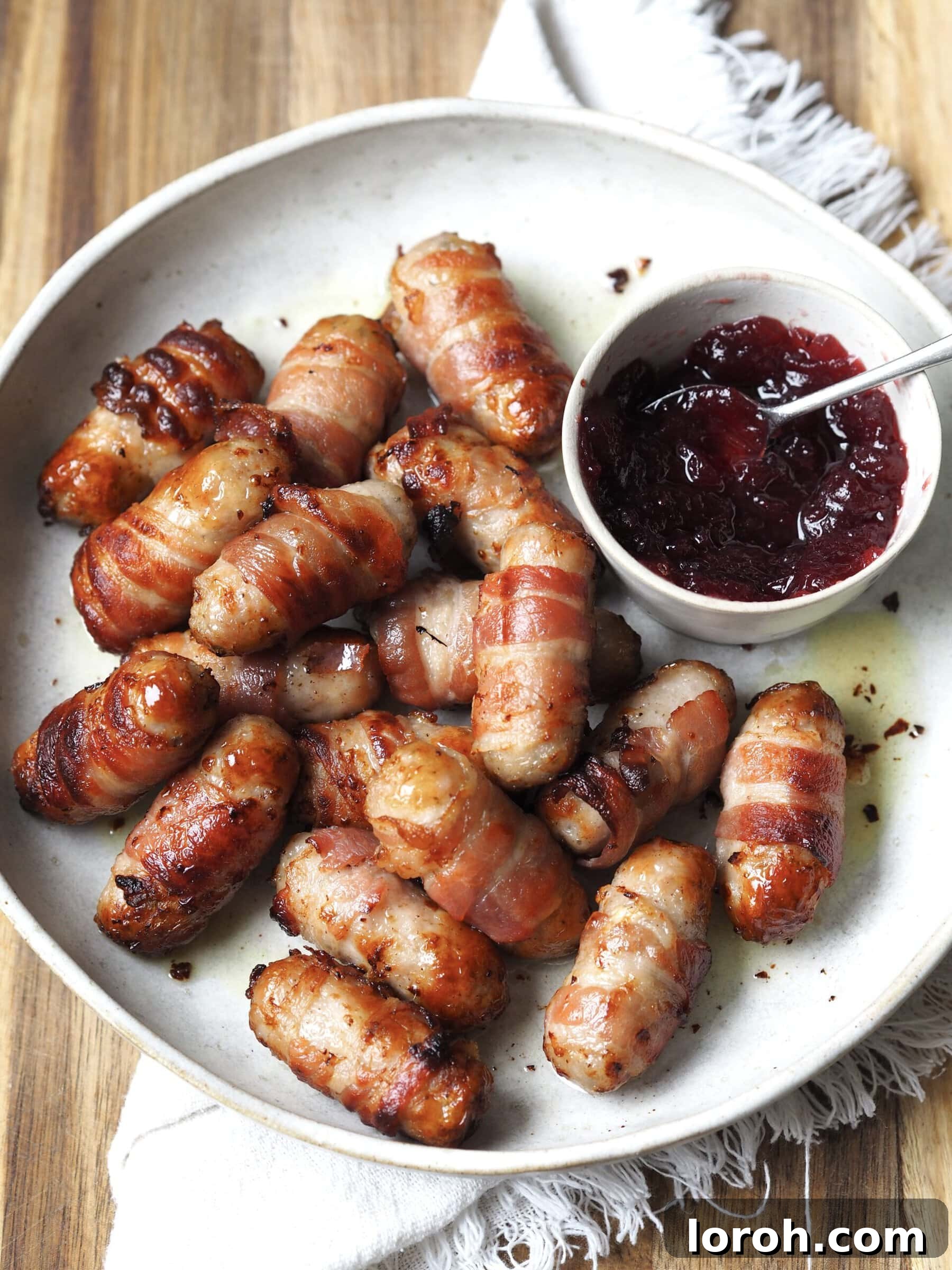 Golden Air Fryer Sausage Bites 2 Close up of a white serving plate of pigs in blankets next to a bowl of cranberry sauce.