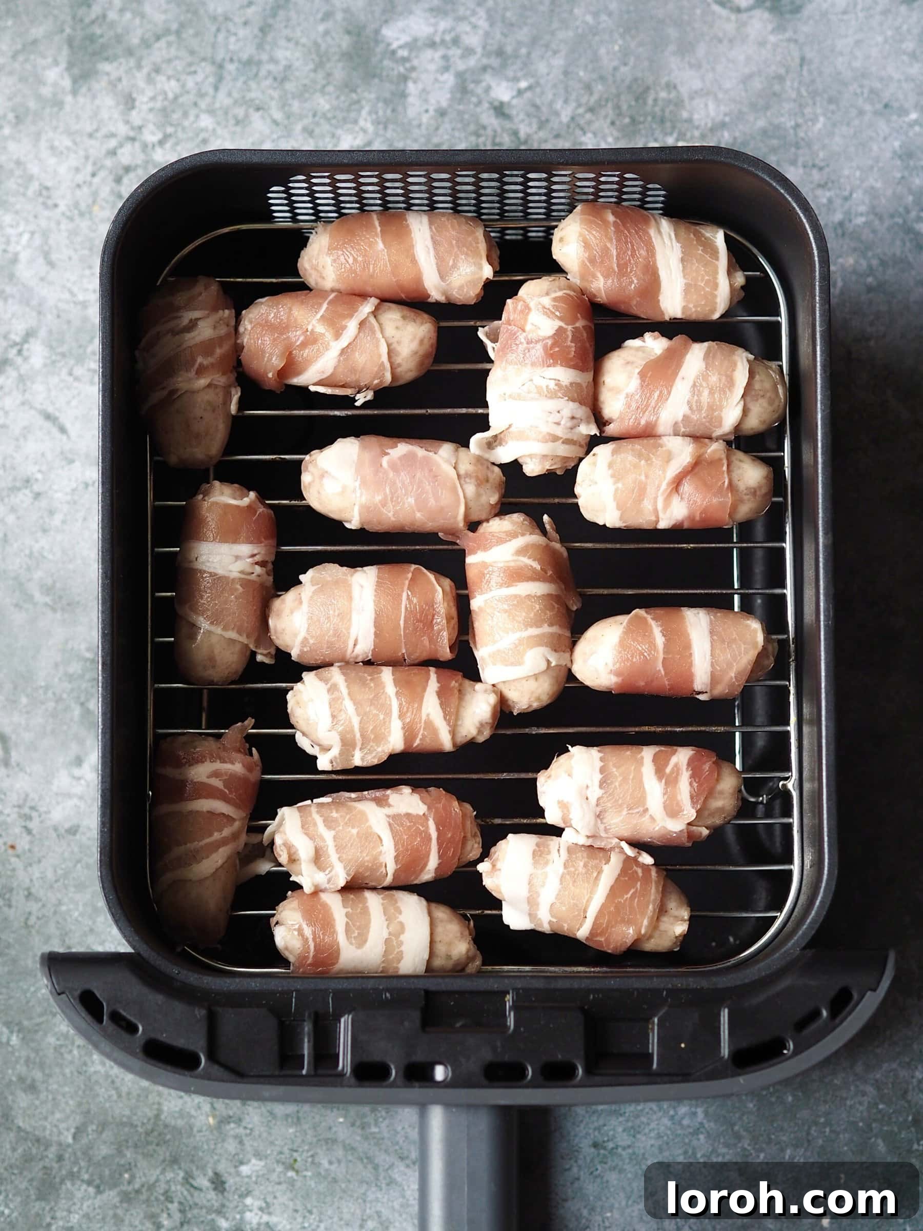 Golden Air Fryer Sausage Bites 5 Uncooked pigs in blankets in an air fryer basket.