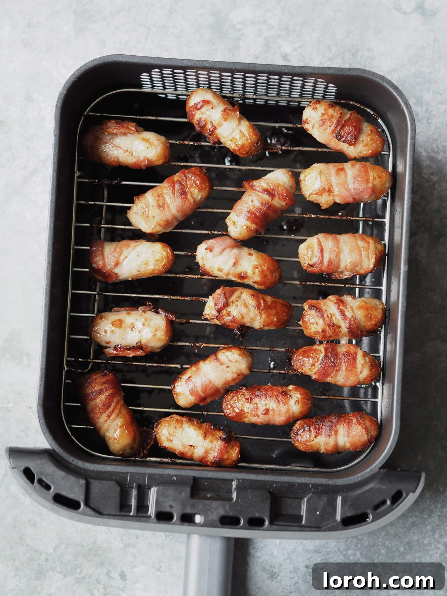 Golden Air Fryer Sausage Bites 6 Cooked pigs in blankets in an air fryer basket.