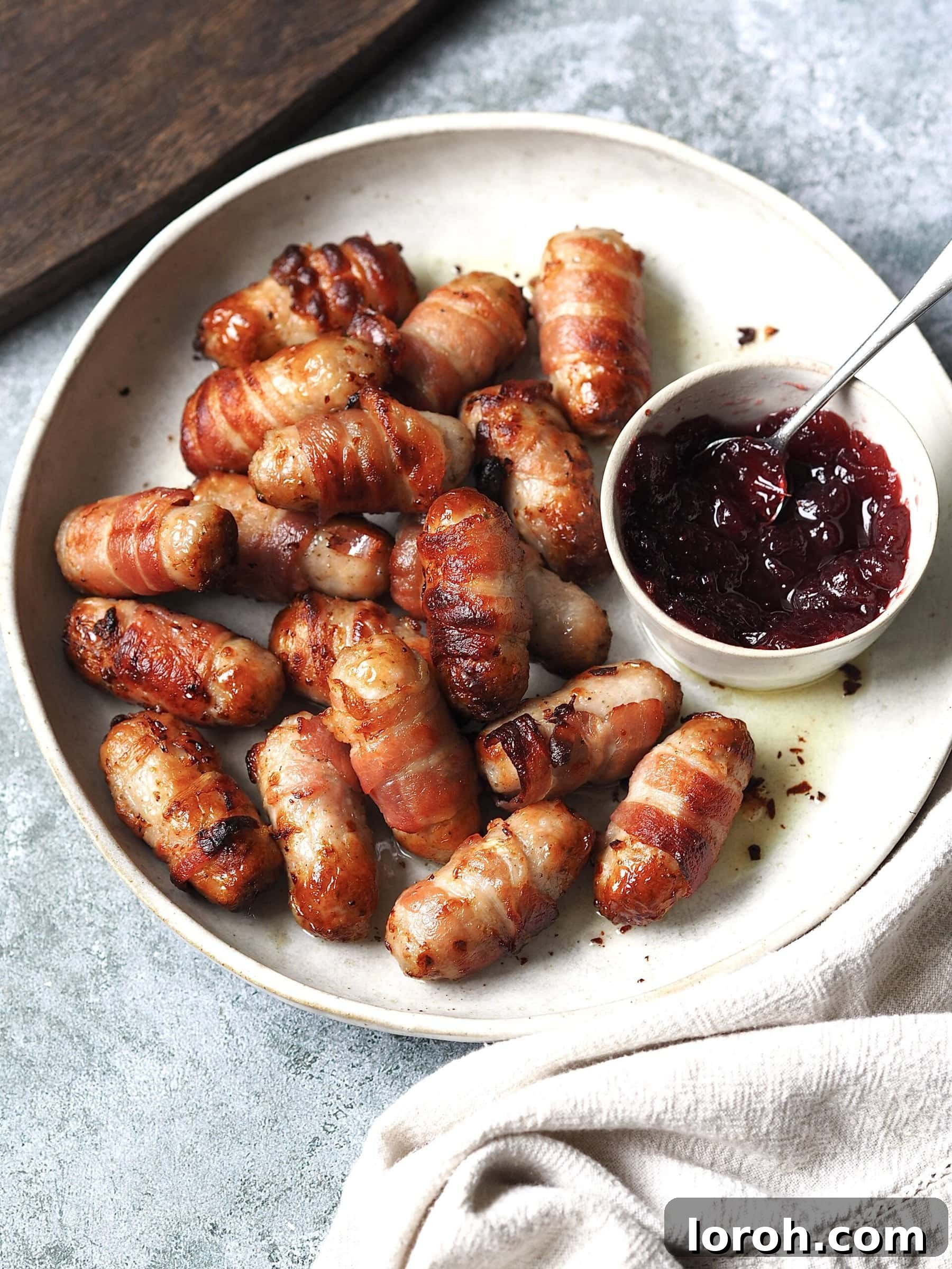 Golden Air Fryer Sausage Bites 8 Pigs in blankets with cranberry sauce on a white serving plate.
