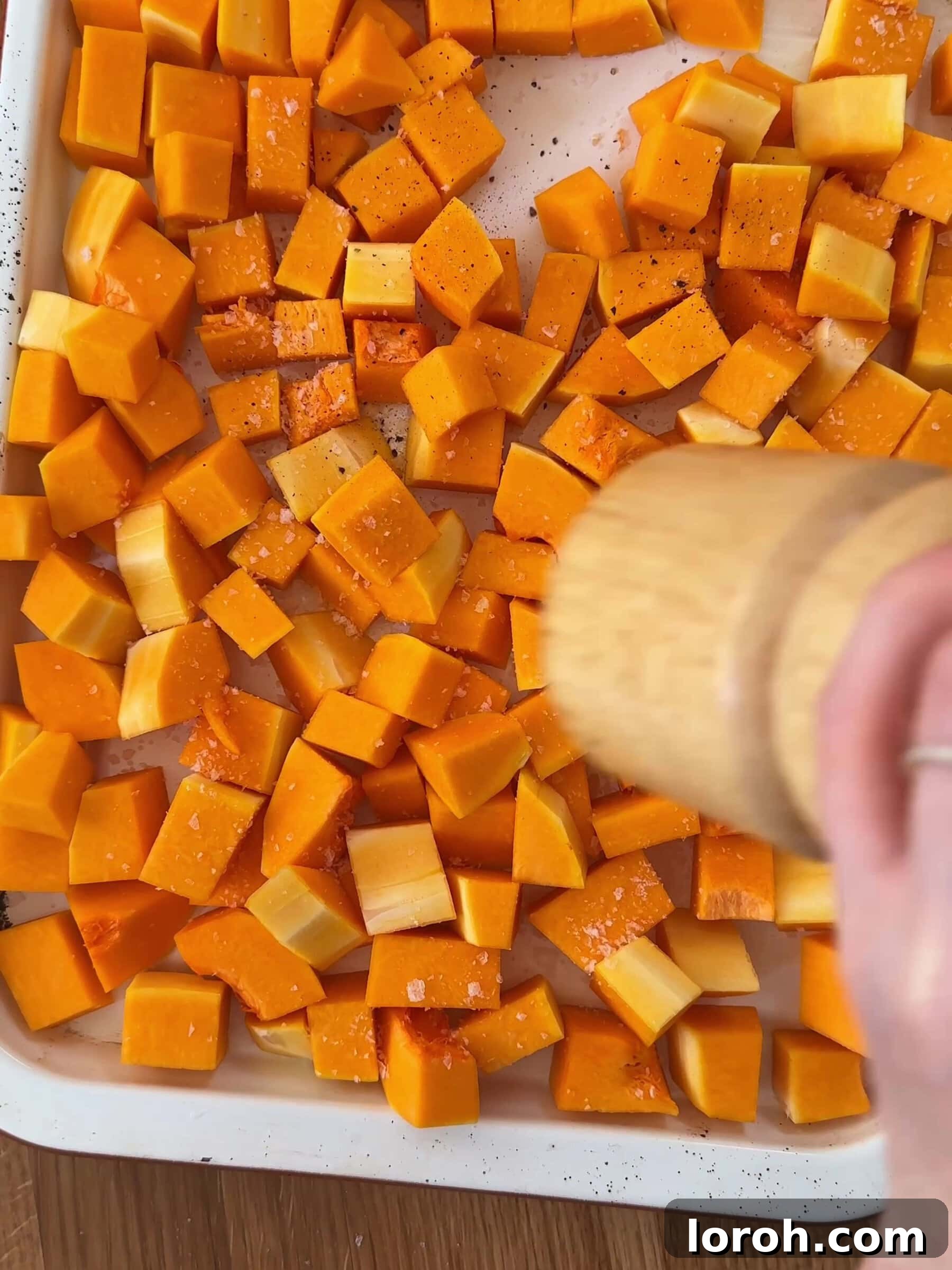 Basil Bliss Lasagna Bake 4 Seasoning diced butternut squash on a baking tray with salt, pepper, and chili flakes.