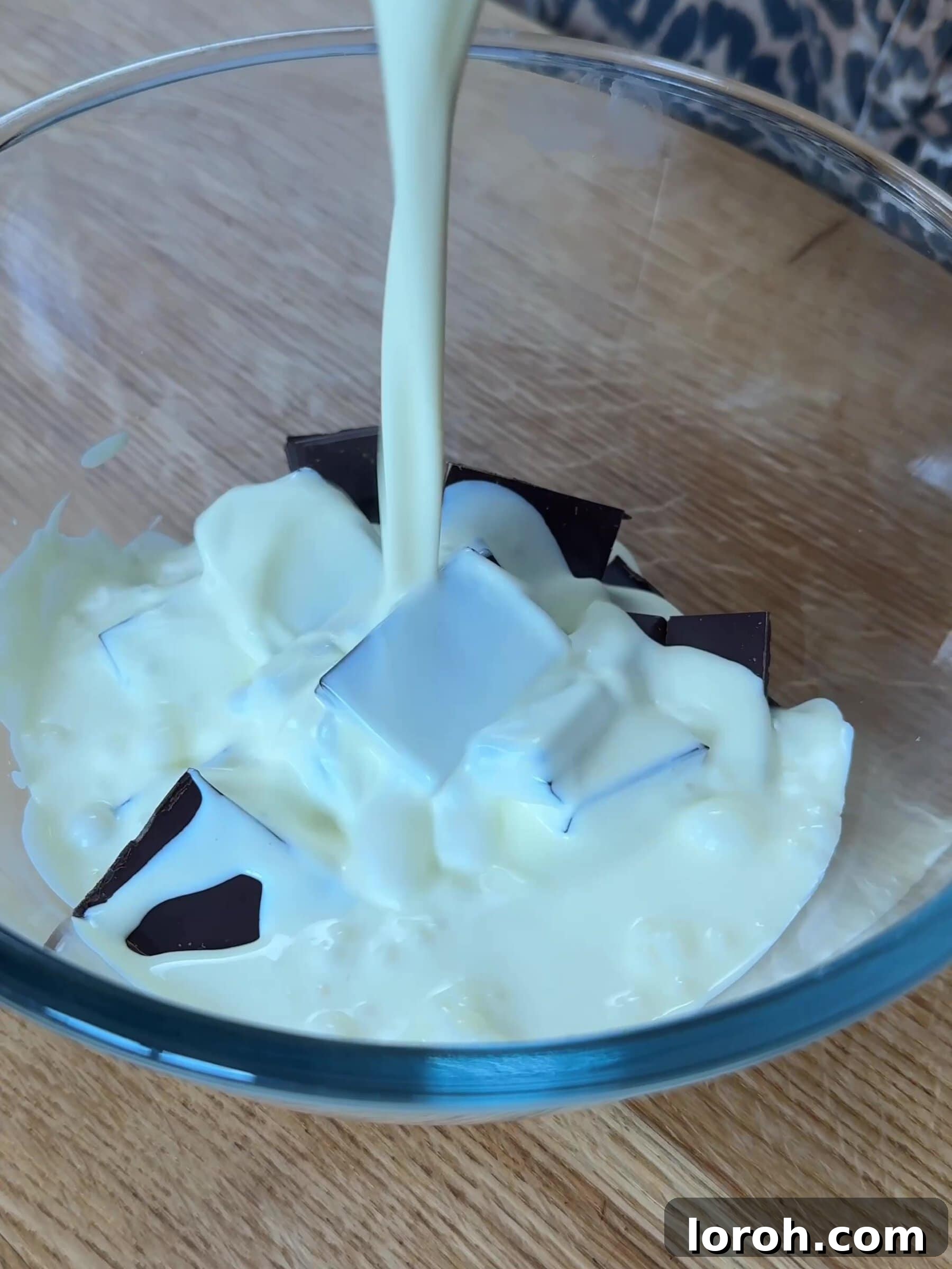 Pouring hot cream over finely chopped dark chocolate in a bowl to make ganache.