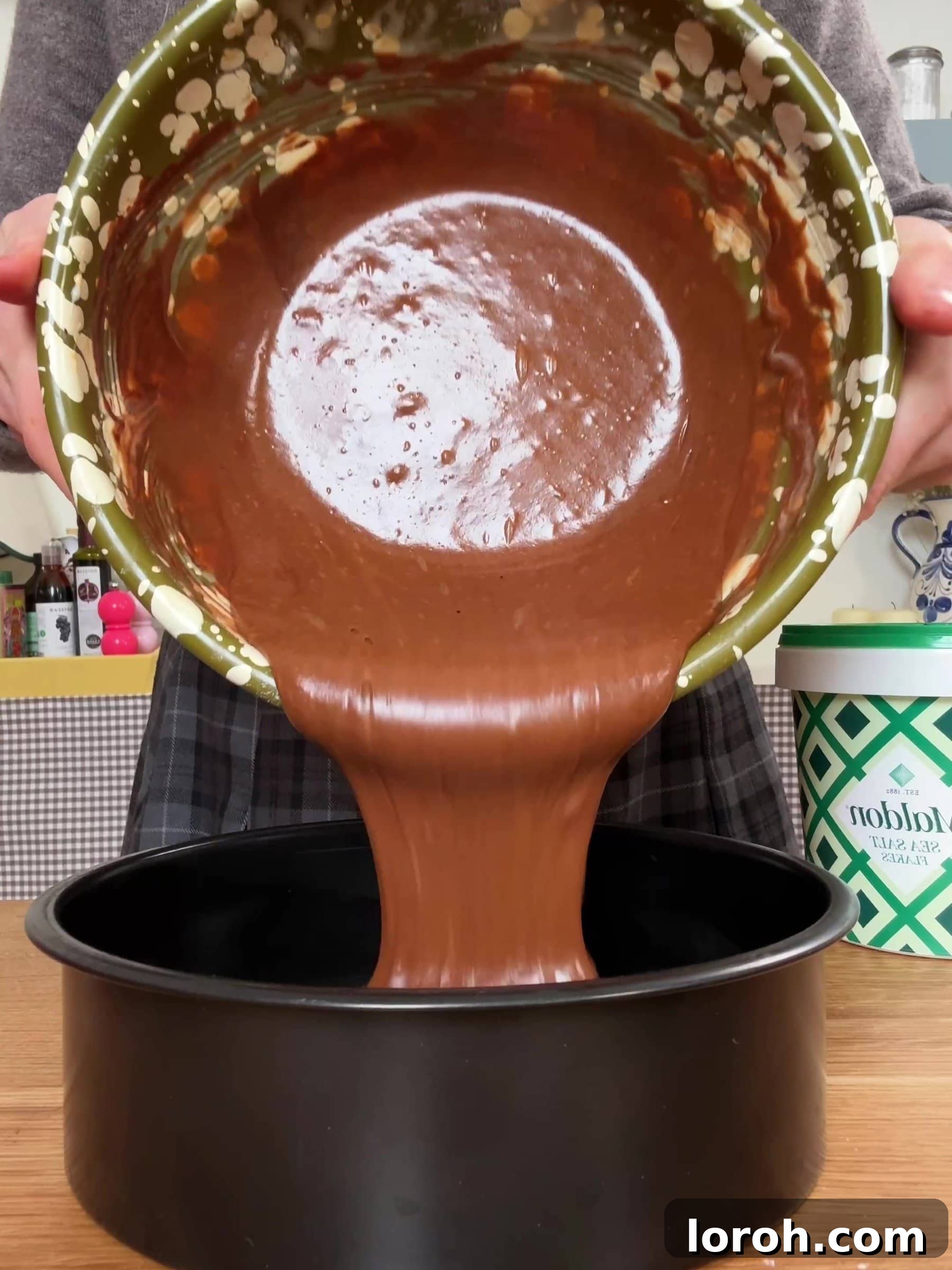 Pouring the smooth chocolate cake batter into the prepared baking tin.