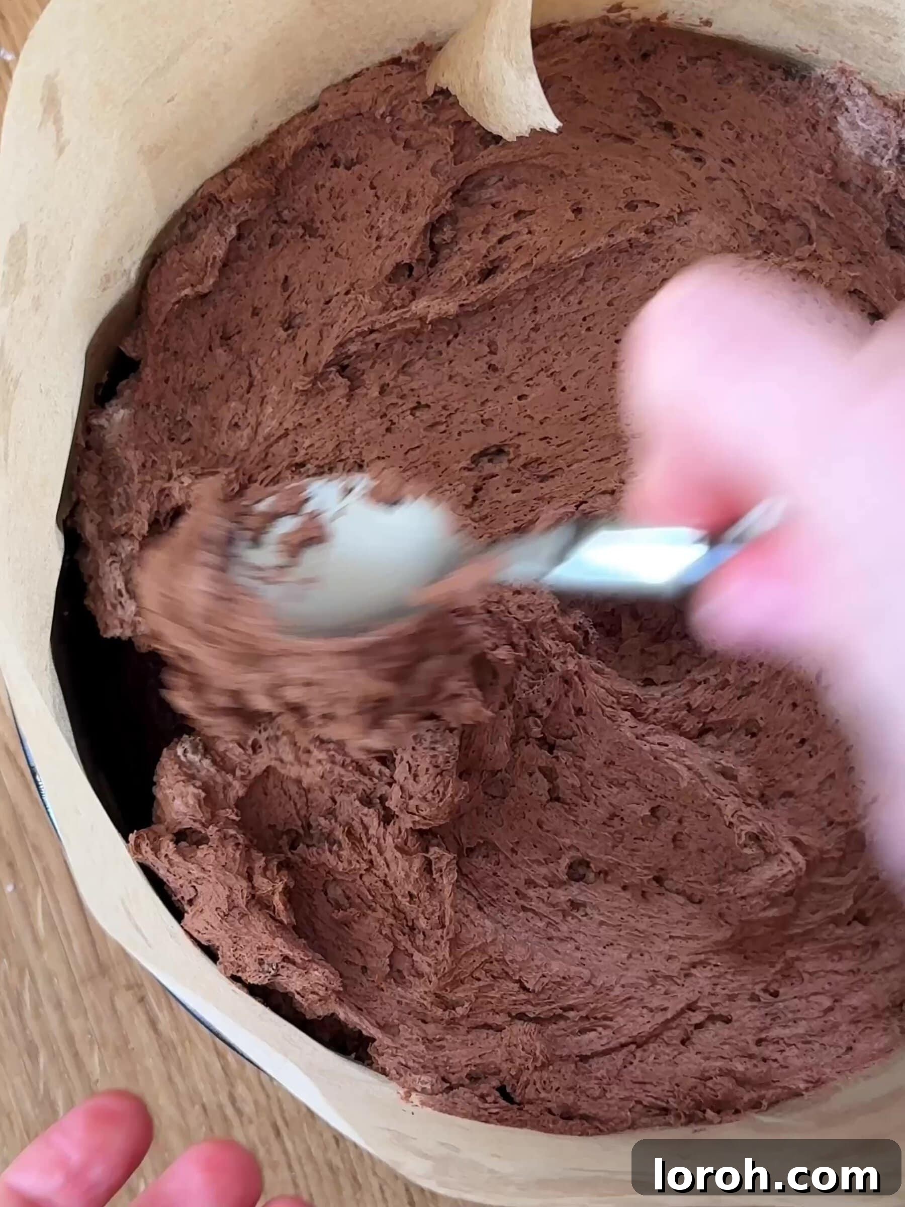 Topping the cooled chocolate cake with a generous layer of chocolate mousse in the cake tin.