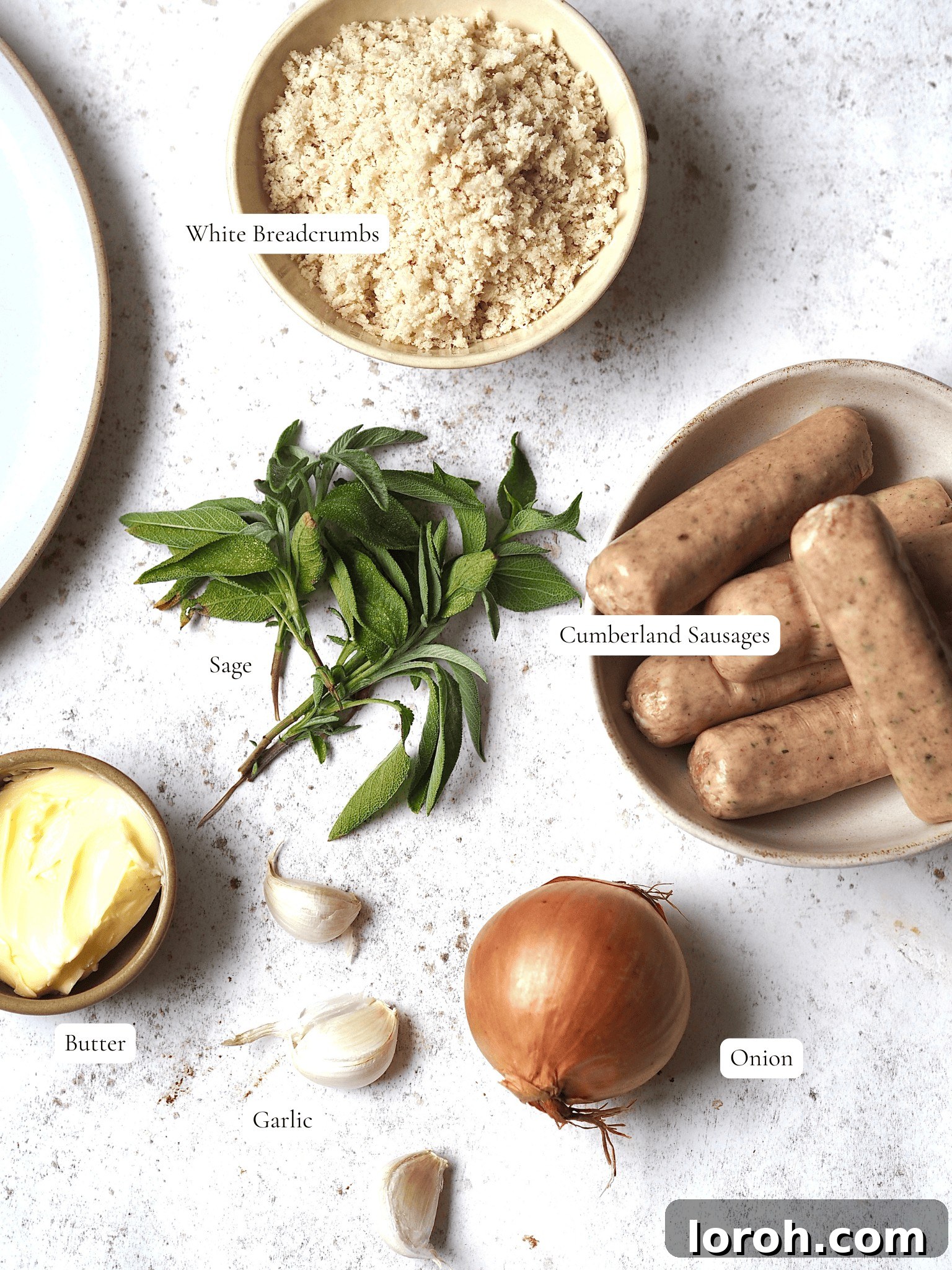Fragrant Sausage, Onion and Sage Stuffing 3 Carefully arranged ingredients for Sausage, Onion, and Sage Stuffing: fresh Cumberland sausages, golden breadcrumbs, a whole onion, garlic cloves, a stick of butter, and fresh sage leaves.