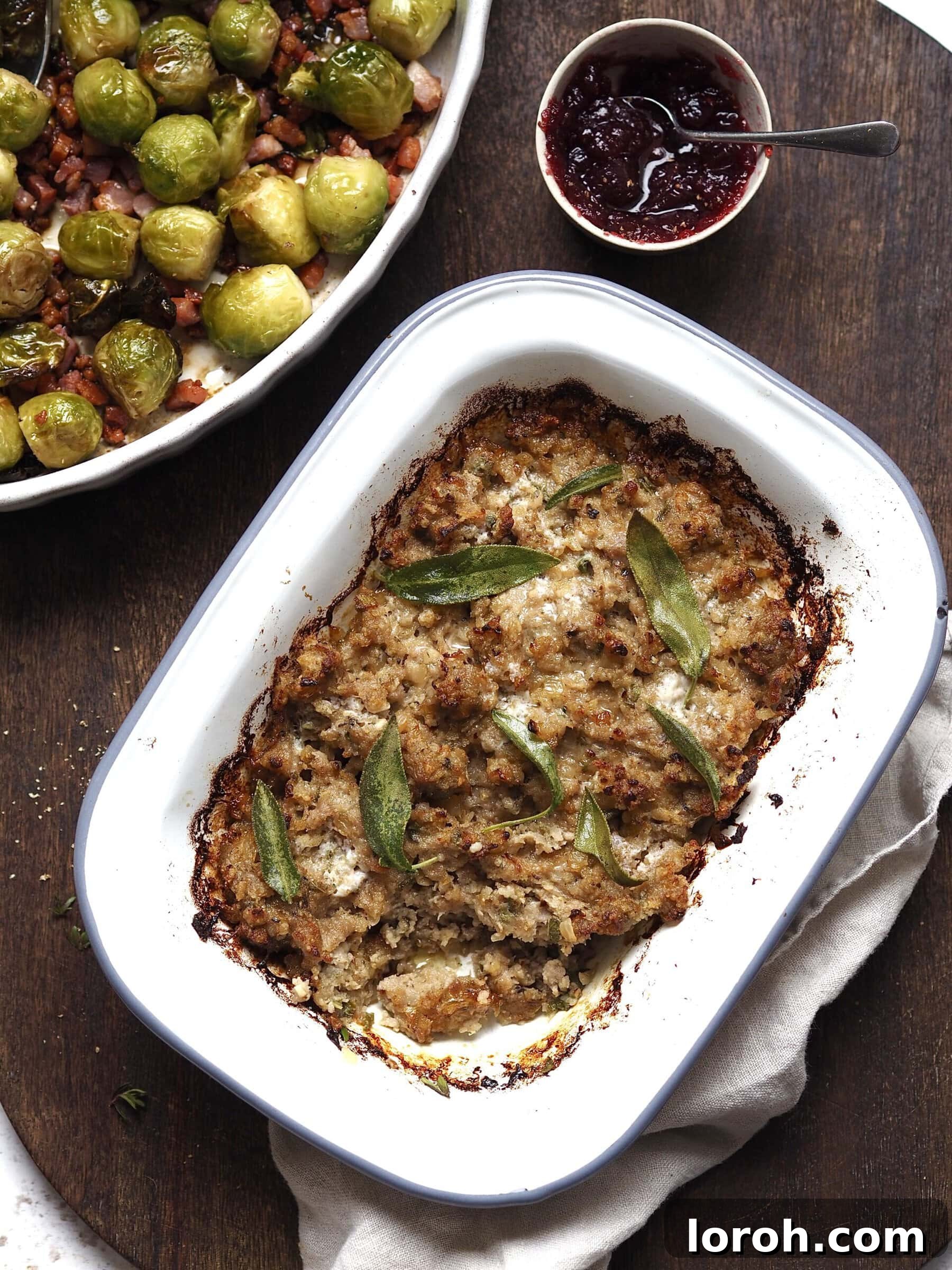 Fragrant Sausage, Onion and Sage Stuffing 4 A large white baking dish filled with golden-brown Sausage, Onion, and Sage Stuffing, served alongside smaller dishes of vibrant green Brussels sprouts and rich red cranberry sauce, embodying a festive holiday spread.