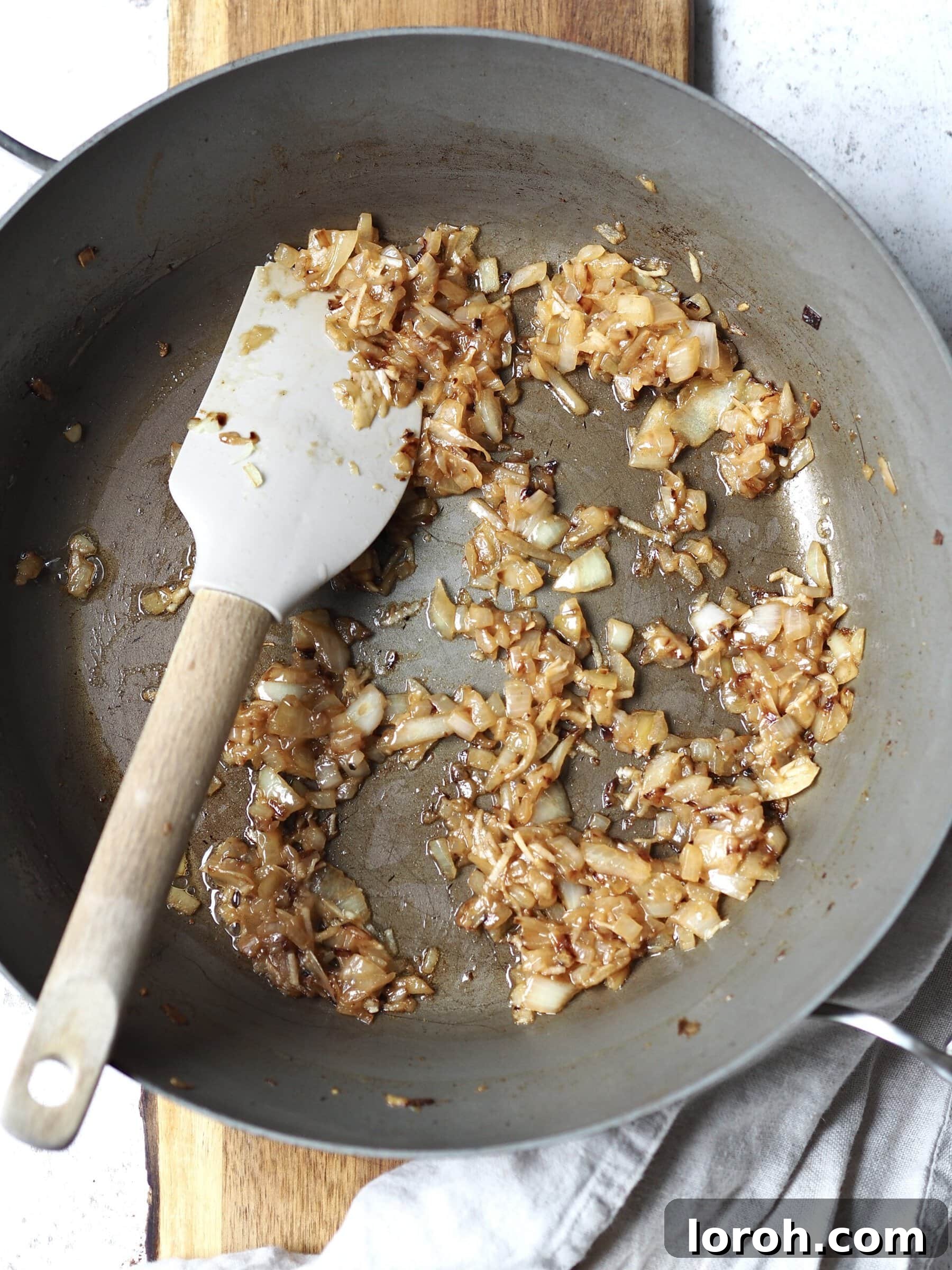 Fragrant Sausage, Onion and Sage Stuffing 5 Diced onions being sautéed in half a portion of butter in a grey frying pan until soft and golden, forming the aromatic base of the stuffing.