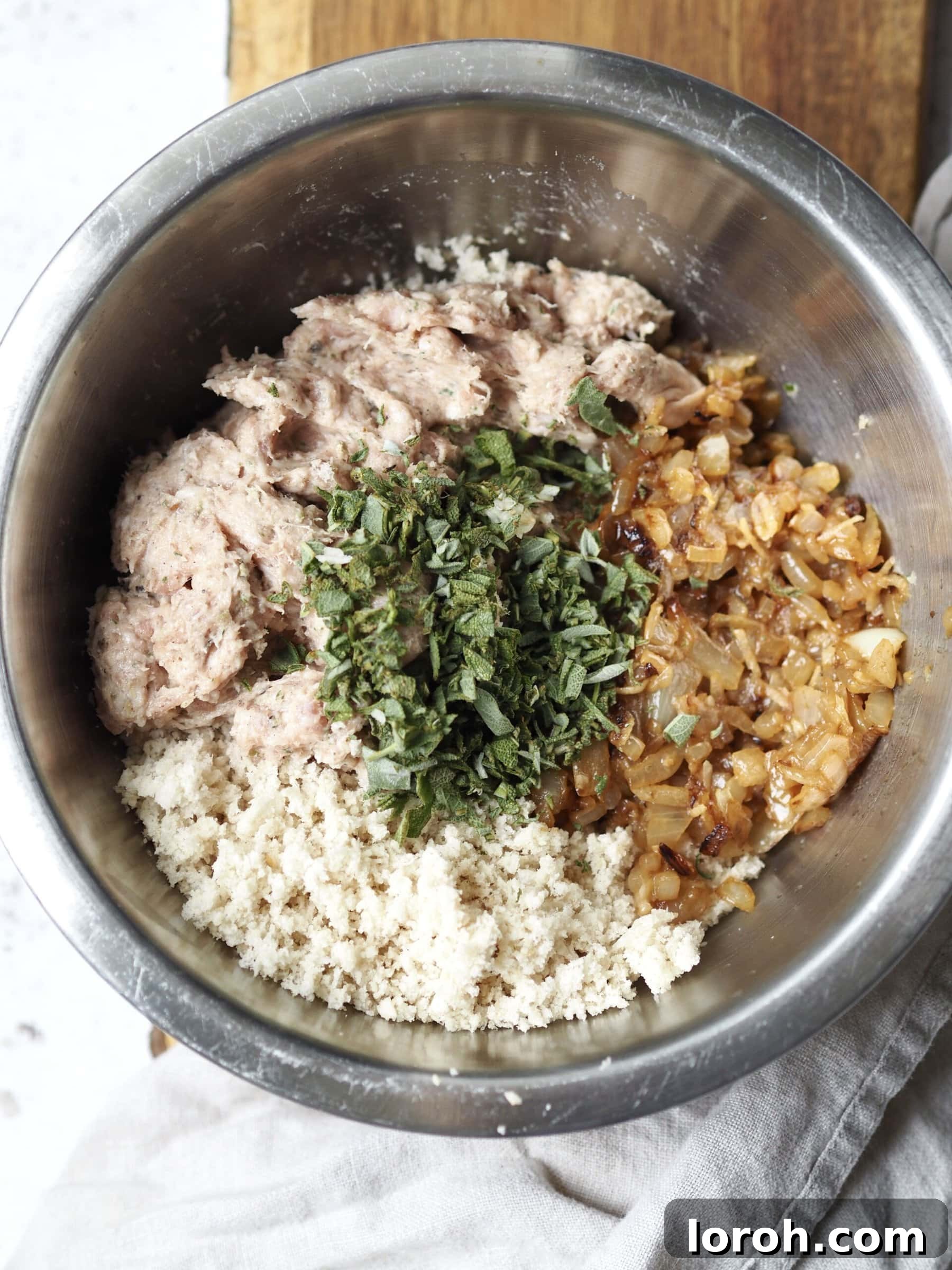 Fragrant Sausage, Onion and Sage Stuffing 6 All the core ingredients for sausage stuffing — raw sausage meat, sautéed onions and garlic, breadcrumbs, and finely chopped fresh sage — combined in a large metal mixing bowl, ready to be thoroughly mixed.