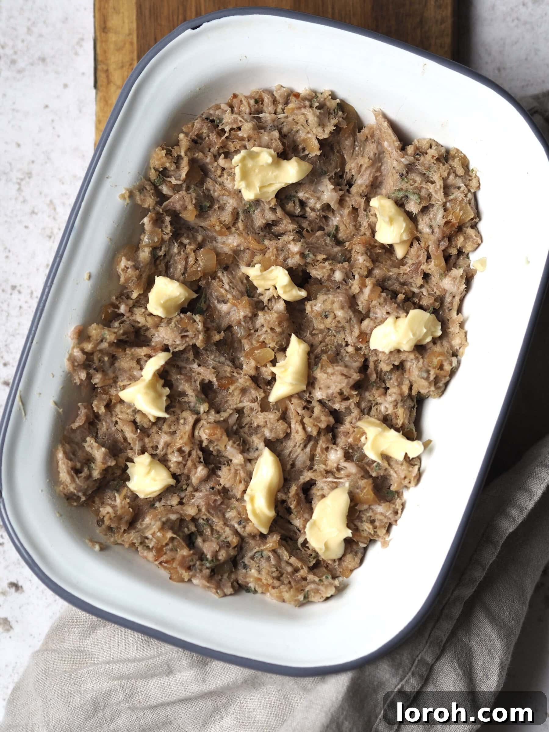 Fragrant Sausage, Onion and Sage Stuffing 7 The raw sausage stuffing mixture, perfectly combined, pressed into a white metal baking dish with its surface ruffled to create crispy bits, and dotted with small cubes of the remaining butter, ready for baking.