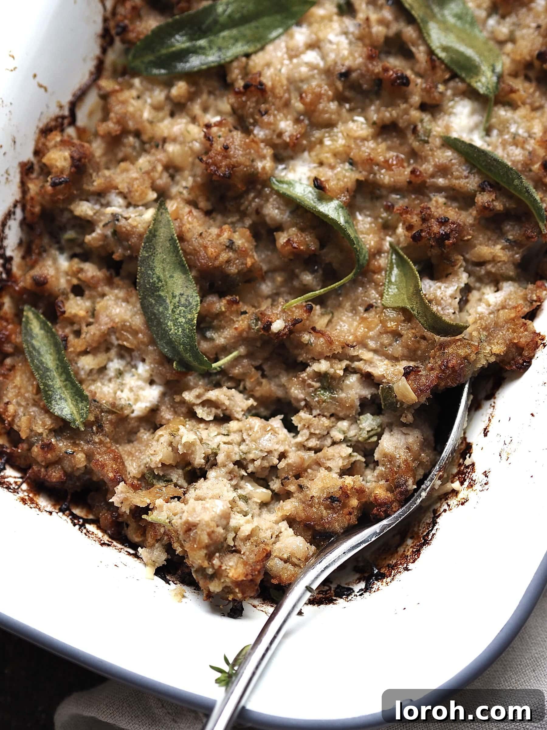 Fragrant Sausage, Onion and Sage Stuffing 9 A close-up image of a serving spoon scooping into a golden-brown dish of Sausage, Onion, and Sage Stuffing, revealing its moist, tender interior and crispy top.