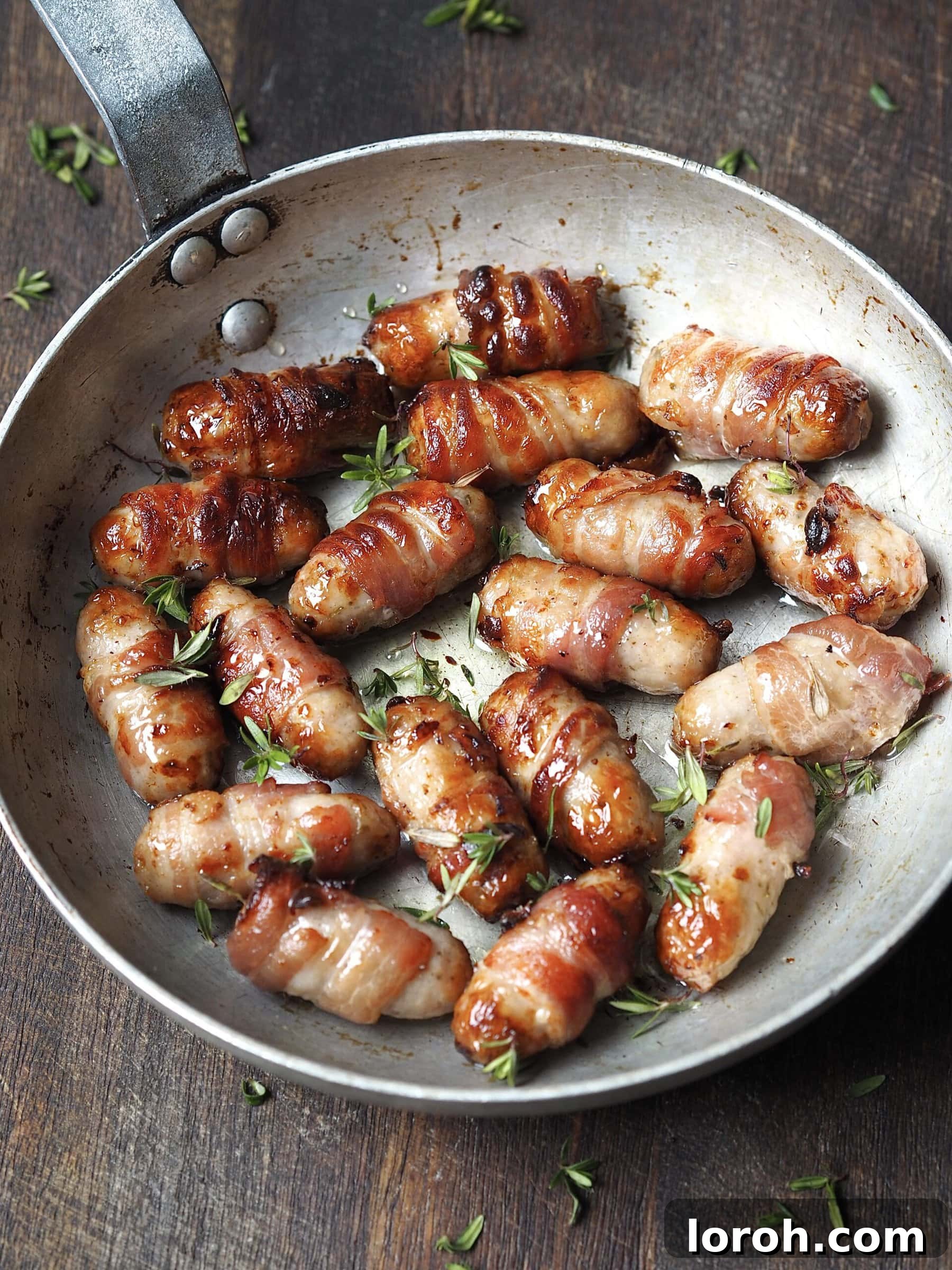 Close up of a metal frying pan of pigs in blankets in a honey and fresh thyme glaze.