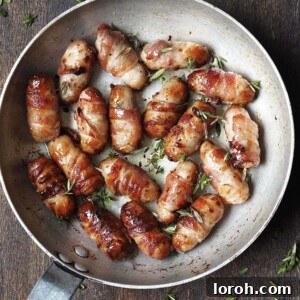 Metal saucepan on a wooden countertop with cooked pigs in blankets with a sticky fresh thyme glaze.