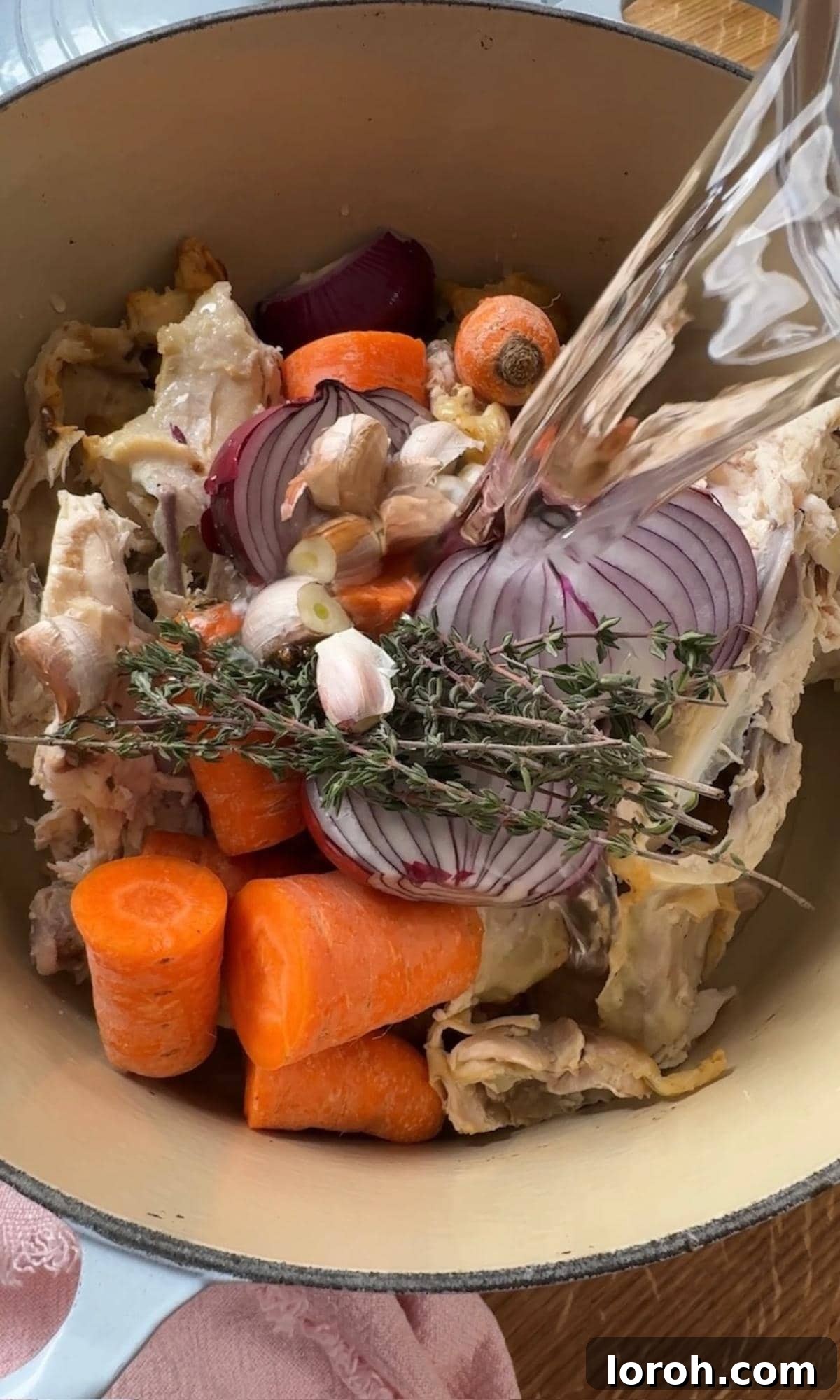 Pouring cold water over chicken carcass and carrots in a pot.