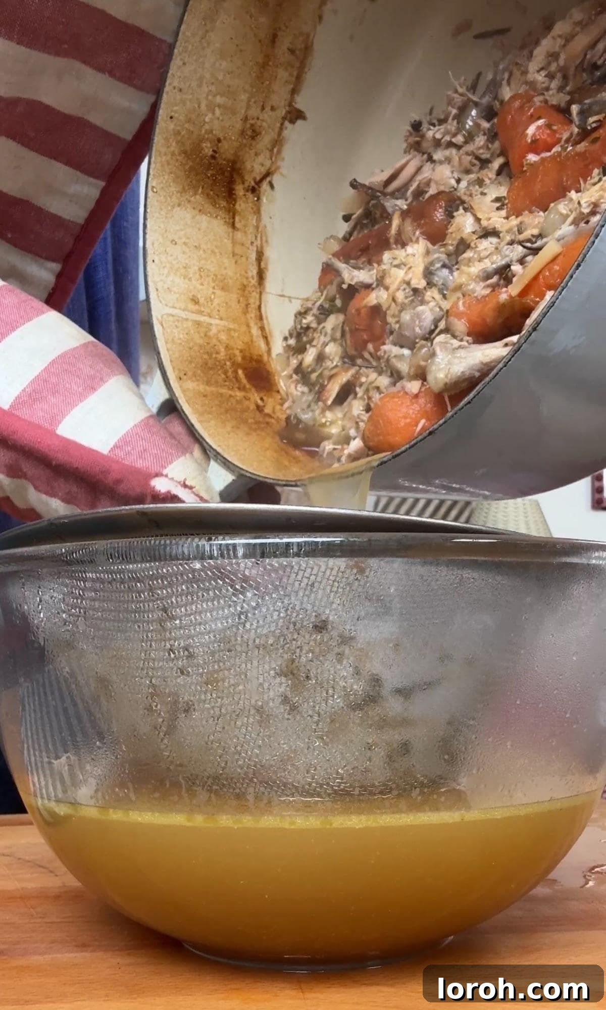 Straining homemade chicken stock through a fine-mesh sieve into a bowl.