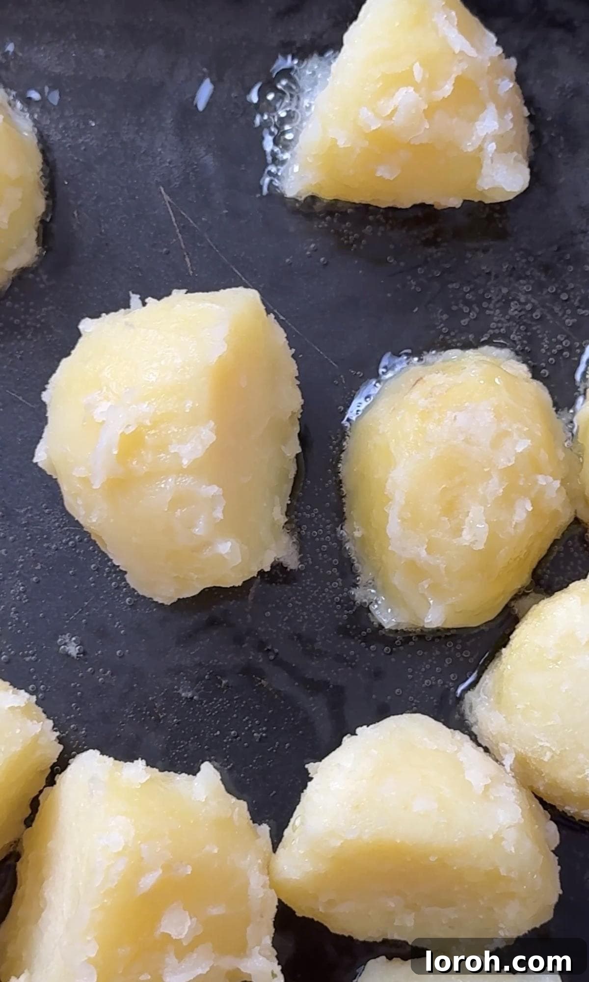 tipping fluffed parboiled potatoes onto hot oil in a baking tray.