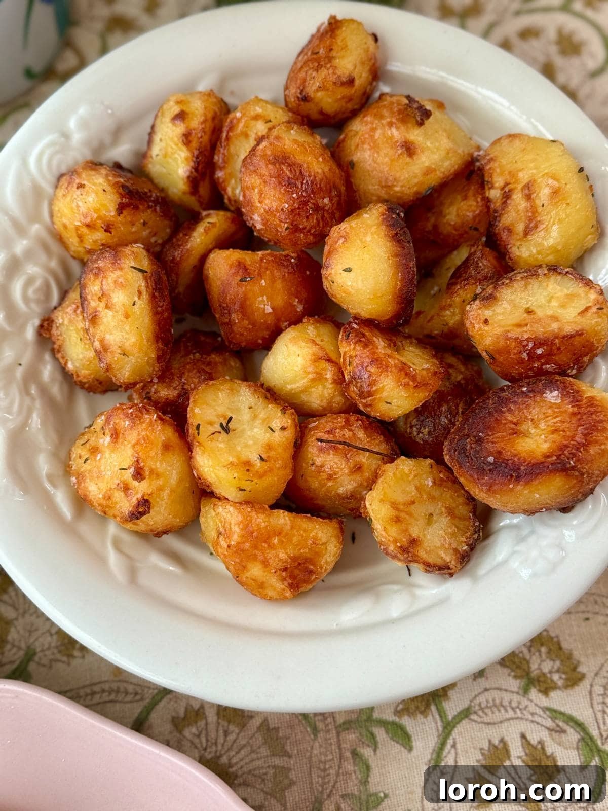 a single white bowl filled with golden crispy roasted white potatoes with rosemary.