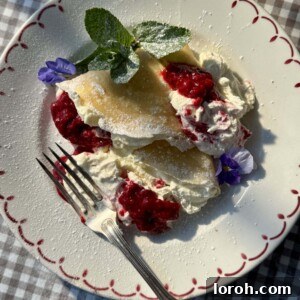 Delicate berry crêpes folded on a white plate, adorned with fresh raspberries and a dollop of creamy cheesecake filling.
