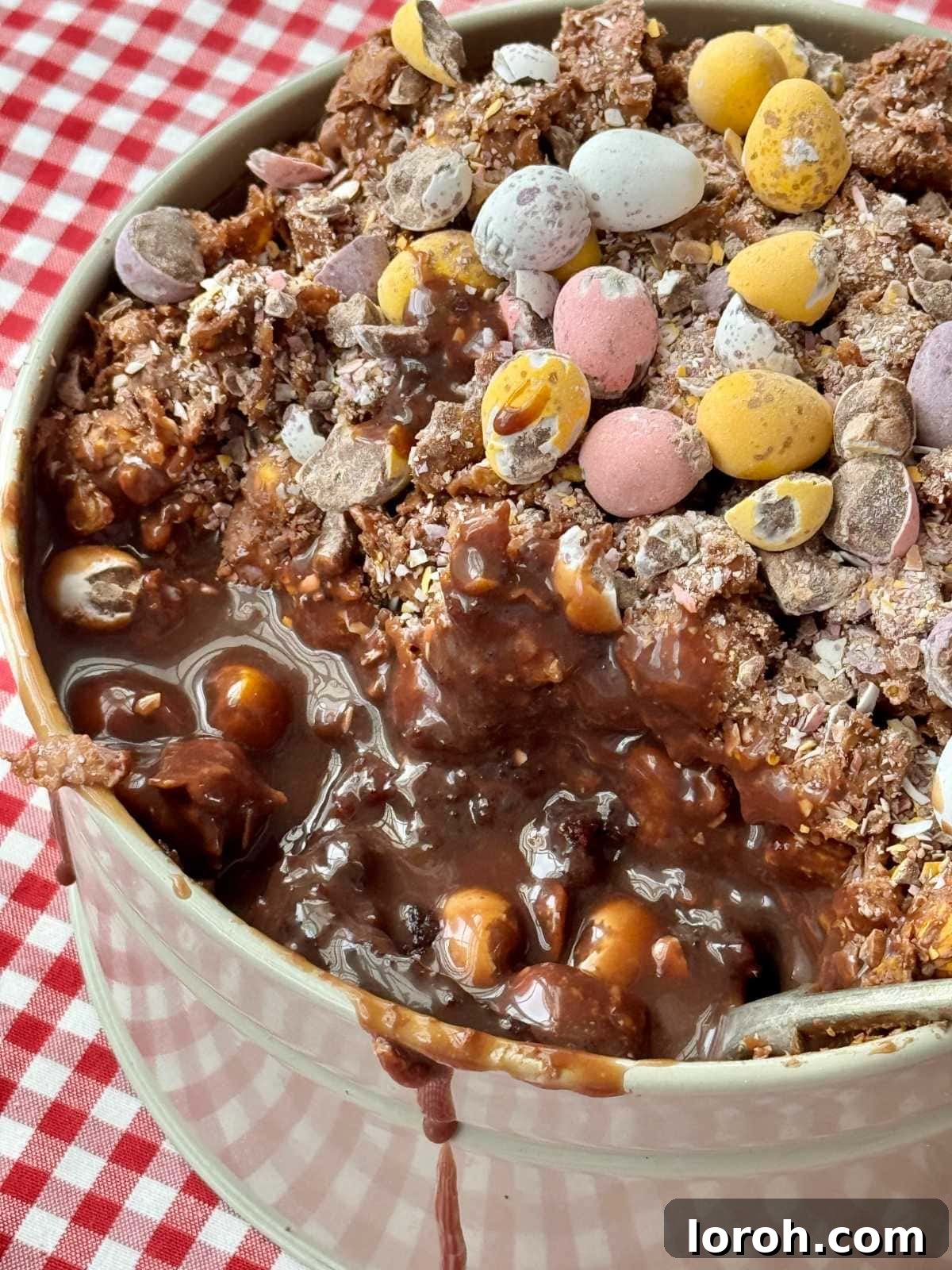 A spoon digging into the rich layers of Cornflake Dream Cake with Mini Eggs, showing the chocolate cake, ganache, and crunchy cornflake topping.