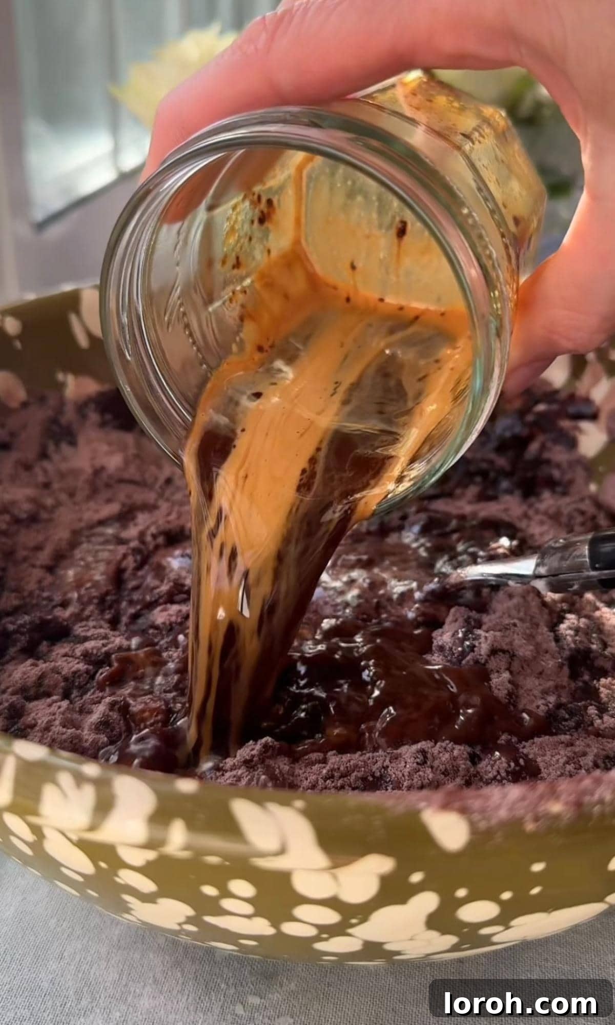 Adding hot coffee to the chocolate cake batter, demonstrating how to gently fold it in.