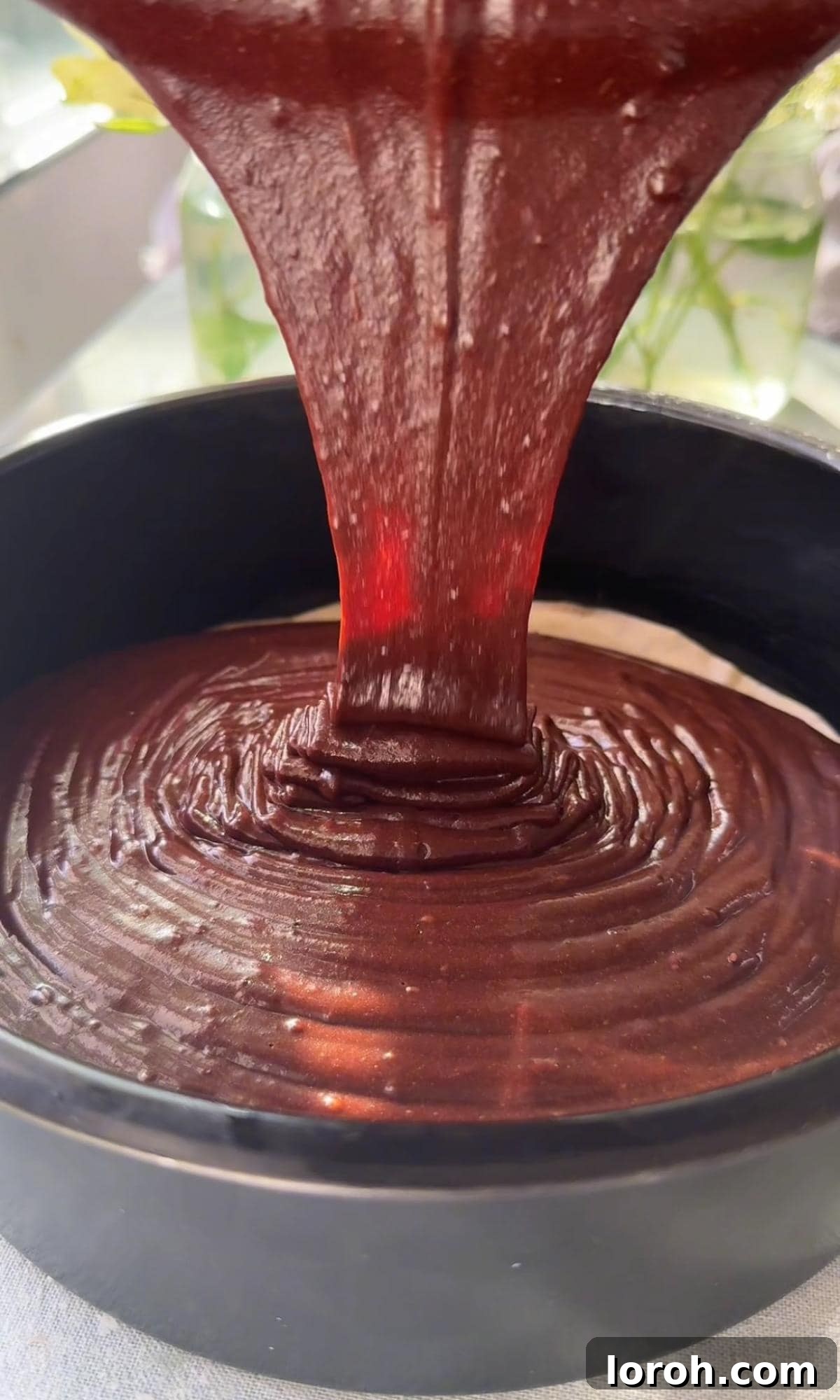 Pouring the rich chocolate cake batter into the prepared deep cake tin, ready for baking.