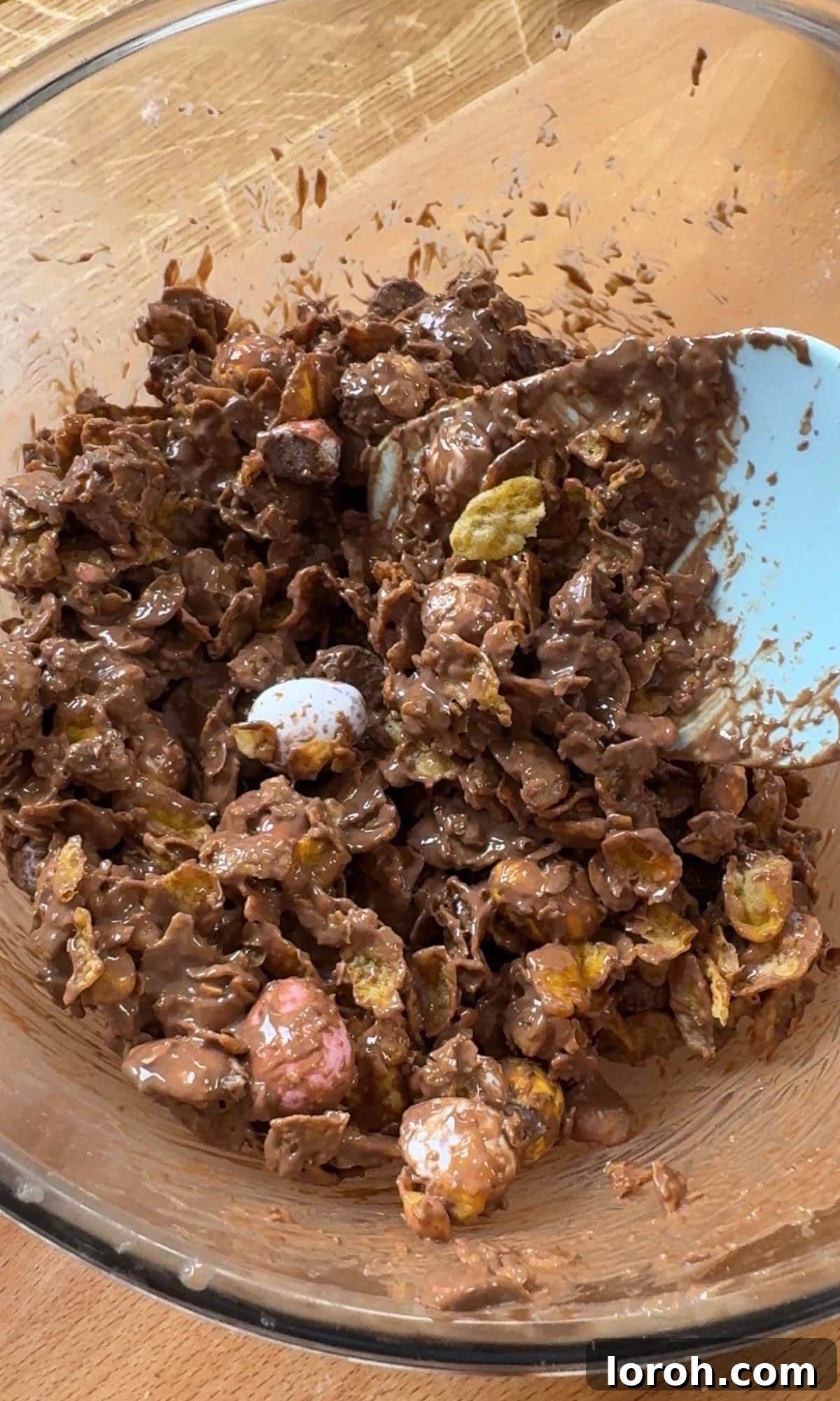 The process of folding cornflakes and crushed mini eggs into melted chocolate for the cake's topping.