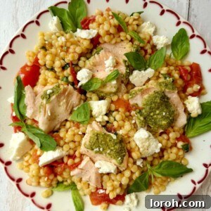 salmon with pesto crust and roasted tomato giant couscous salad on a plate.