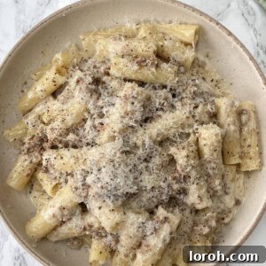 creamy sausage pasta in a beige bowl covered in a grating of cheese.