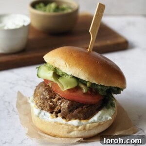 Lamb burger with tomato, cucumber ribbons, tzatziki and pesto on a white marble countertop.