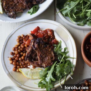 air fryer lamb chops with tomato aubergine stew and rocket on a white plate.