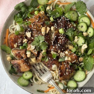 pork belly noodles in a white bowl decorated with herbs and cucumber