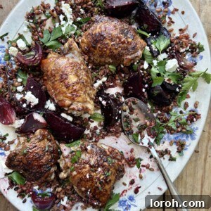 Blue and white serving platter of roasted chicken thighs, beetroot and red onion over mixed grains.