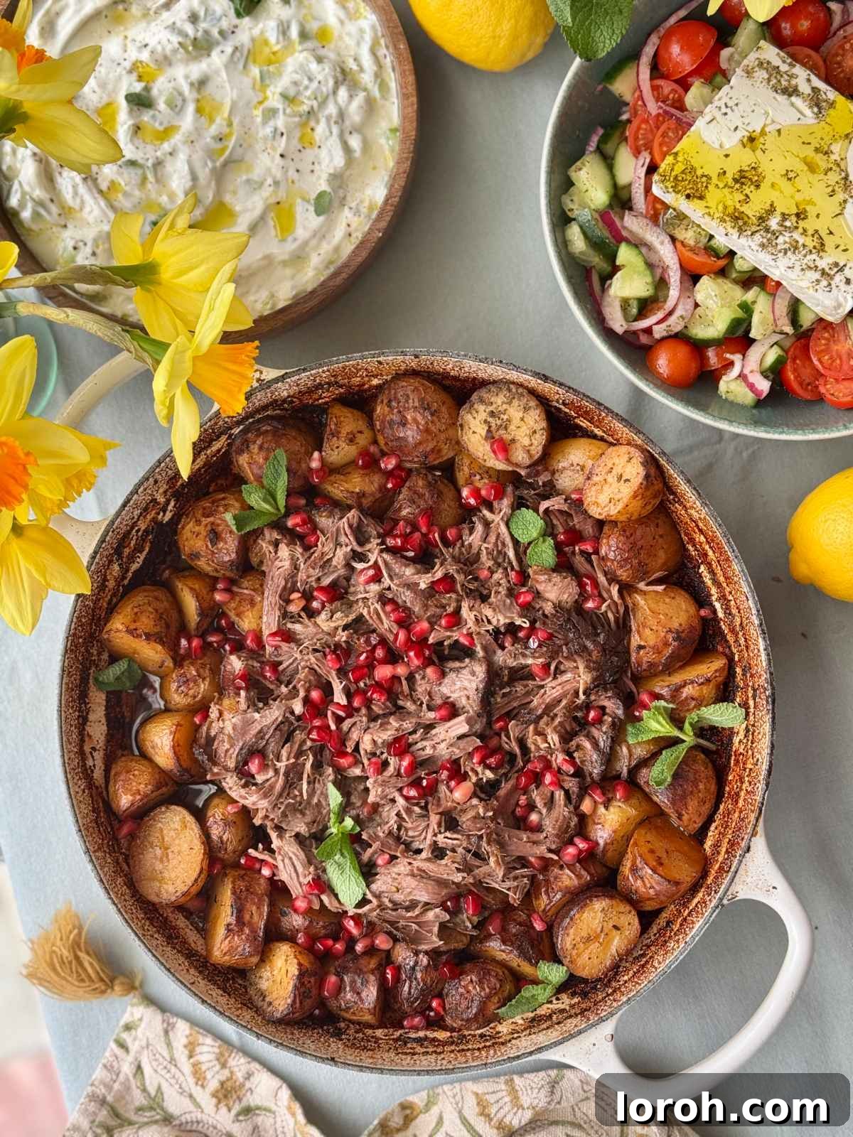 Slow cooked lamb leg with roasted baby potatoes and pan juices in a large roasting tray, ready to serve.