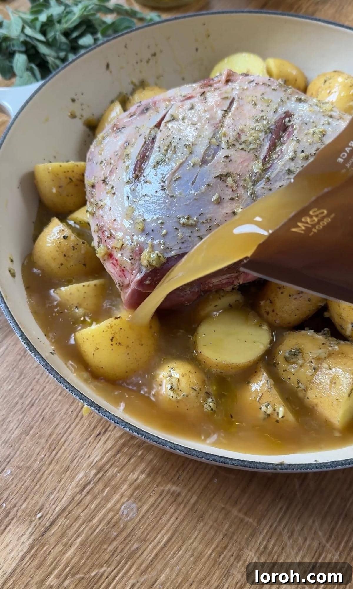 Pouring chicken stock and white wine into the roasting pan, around the lamb and over the potatoes.