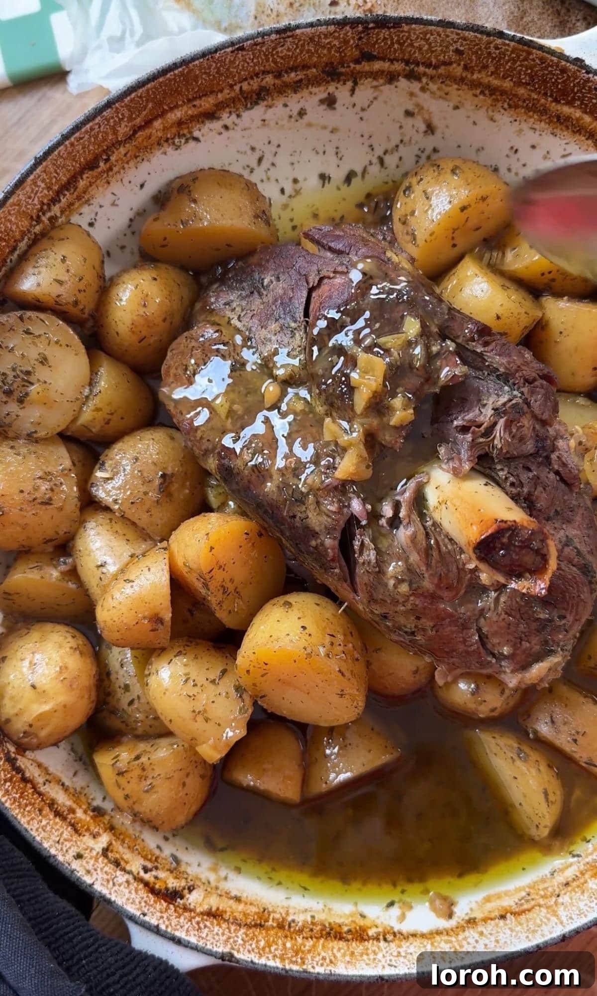 Basting the golden-brown slow cooked lamb leg with pan juices after removing the lid.