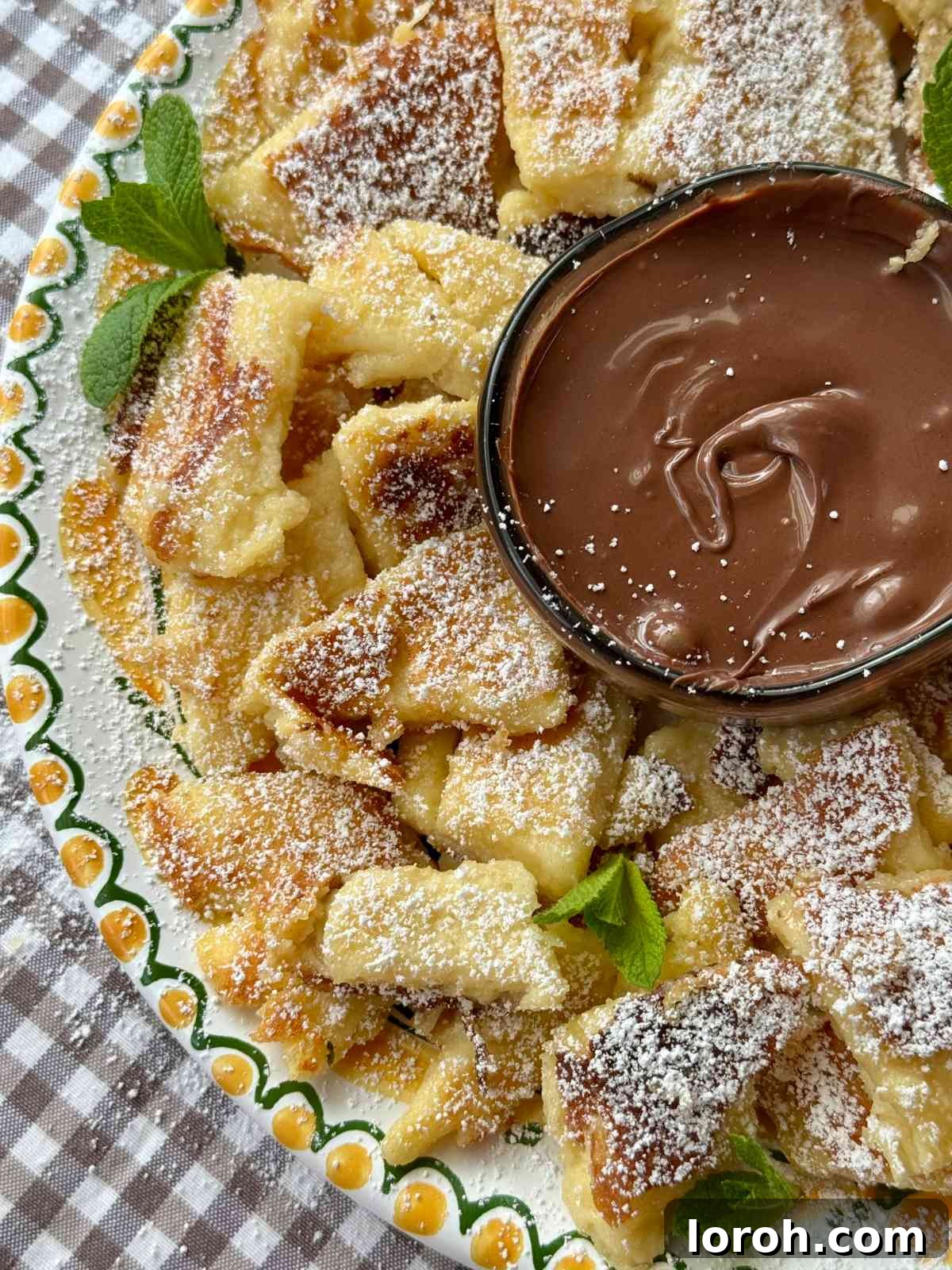 A close-up of Kaiserschmarrn pieces, golden and caramelized, on a white plate with powdered sugar and berries.