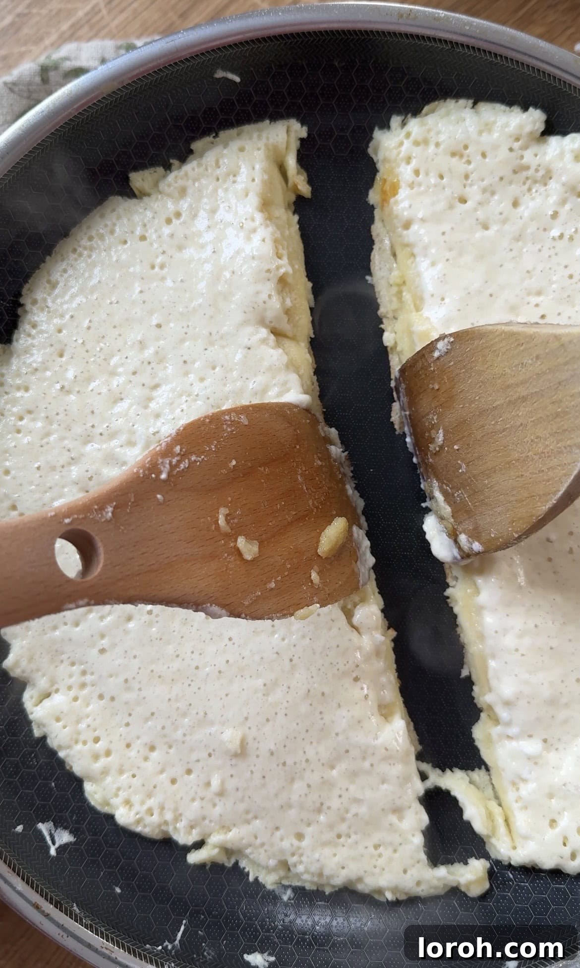 Thick pancake batter cooking gently in a large frying pan, forming a golden base.