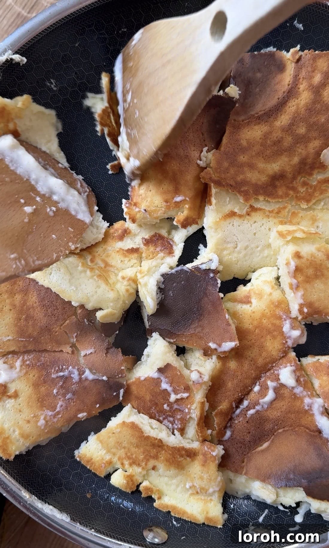 Using two spatulas to tear the cooking pancake into rough, bite-sized pieces directly in the frying pan.