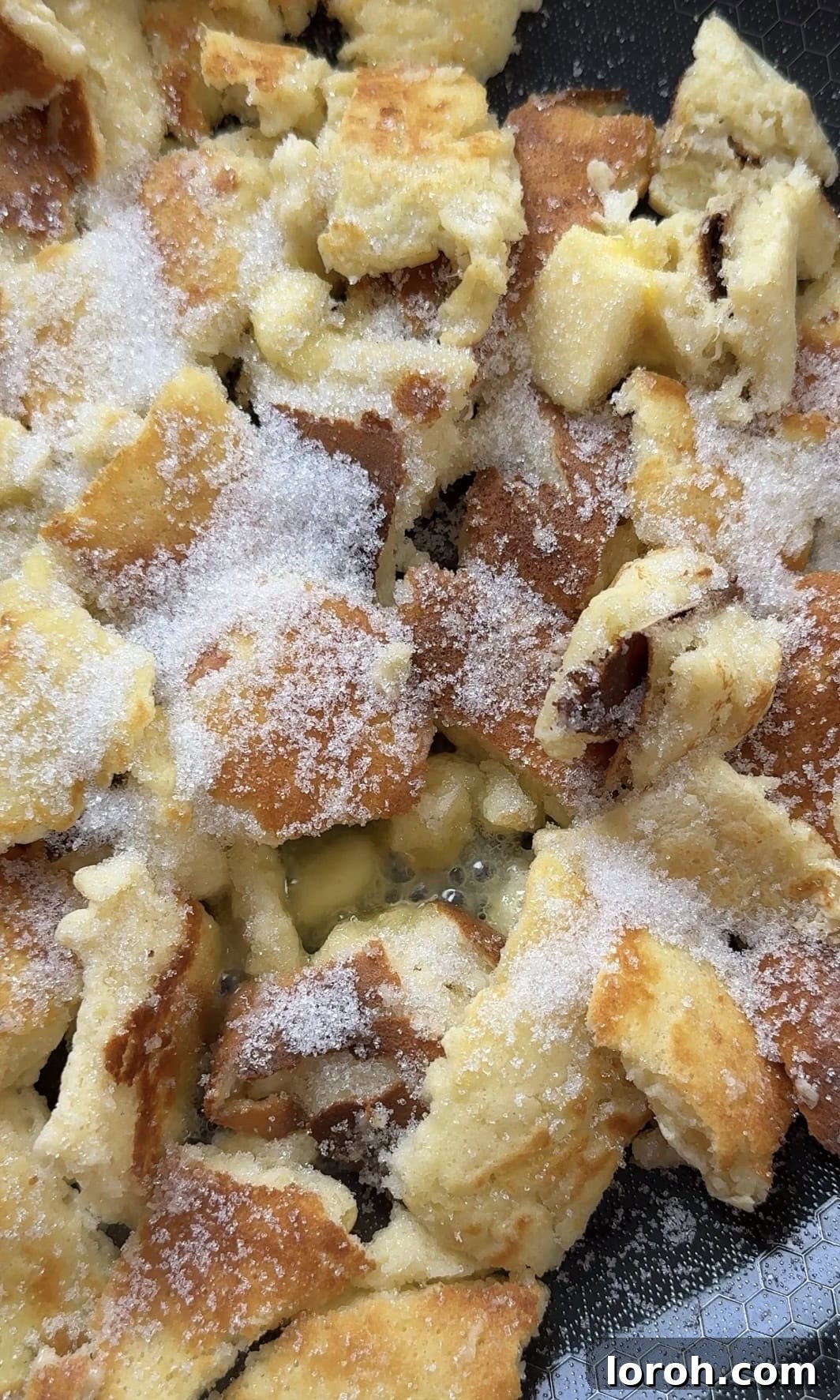 Adding more butter and granulated sugar to the torn Kaiserschmarrn pieces in the pan for caramelization.